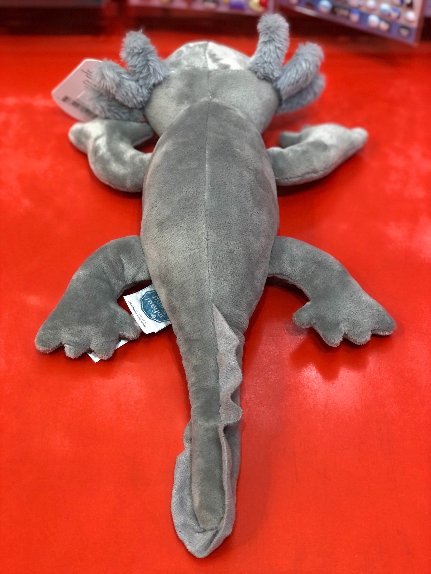 Soft gray axolotl plush toy on red background, showcasing unique features and cuddly design for children's play
