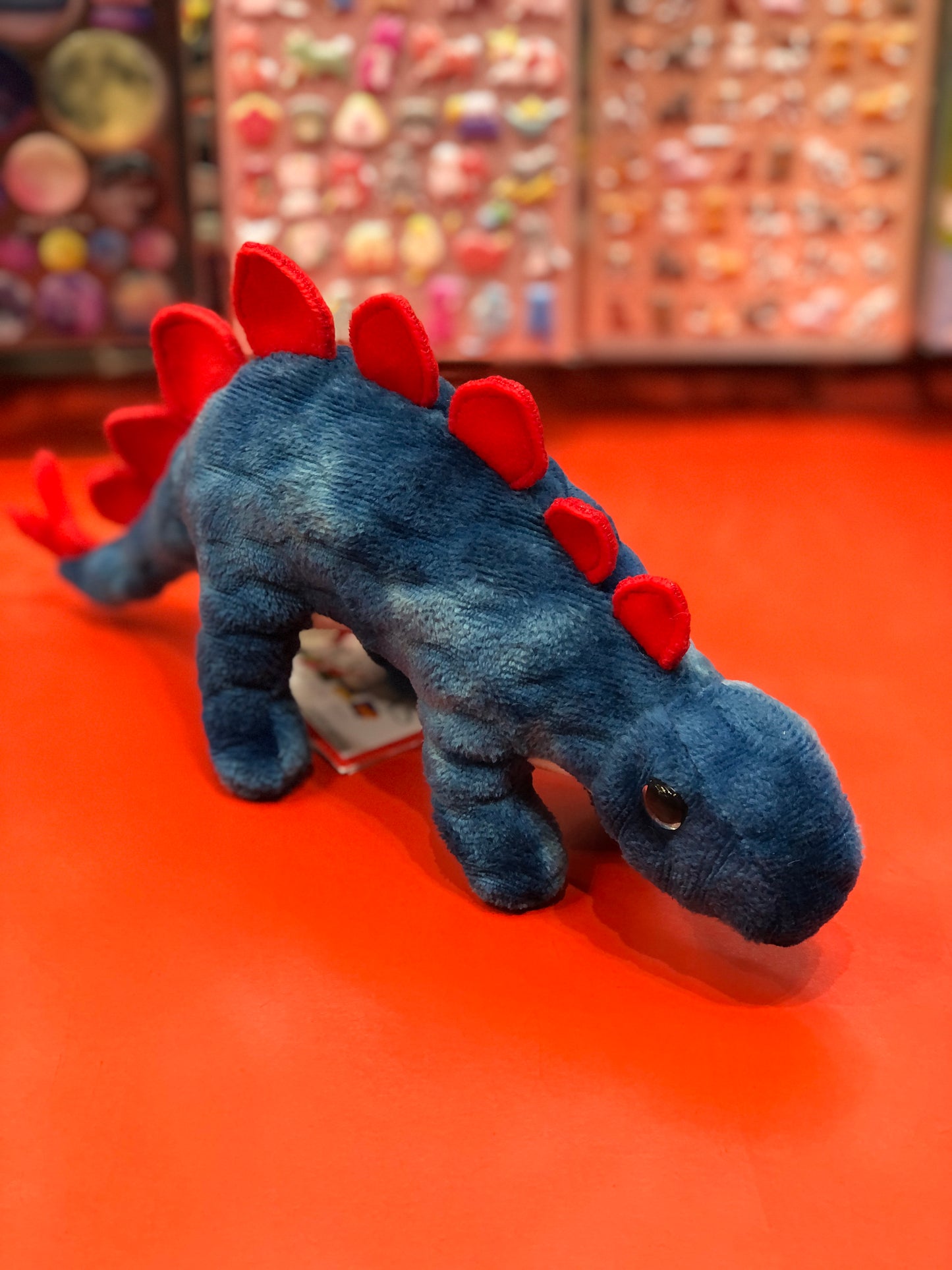 Cute blue Spinosaurus plush toy with red spikes on display, featuring soft velvet texture and lively expression