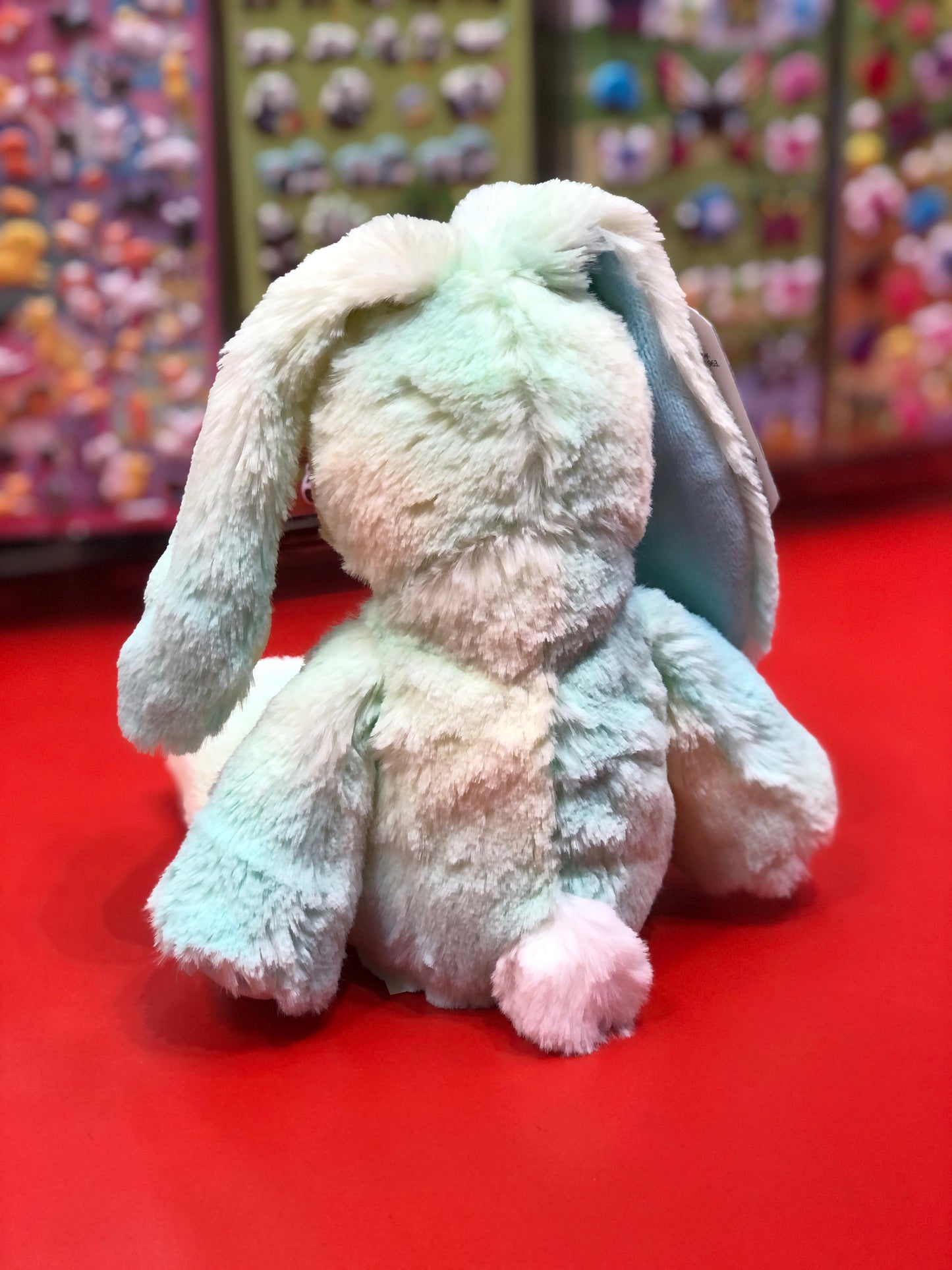 Soft pastel Jellybean Bunny plush toy from Marshmallow Zoo on red display, colorful stuffed animals in background