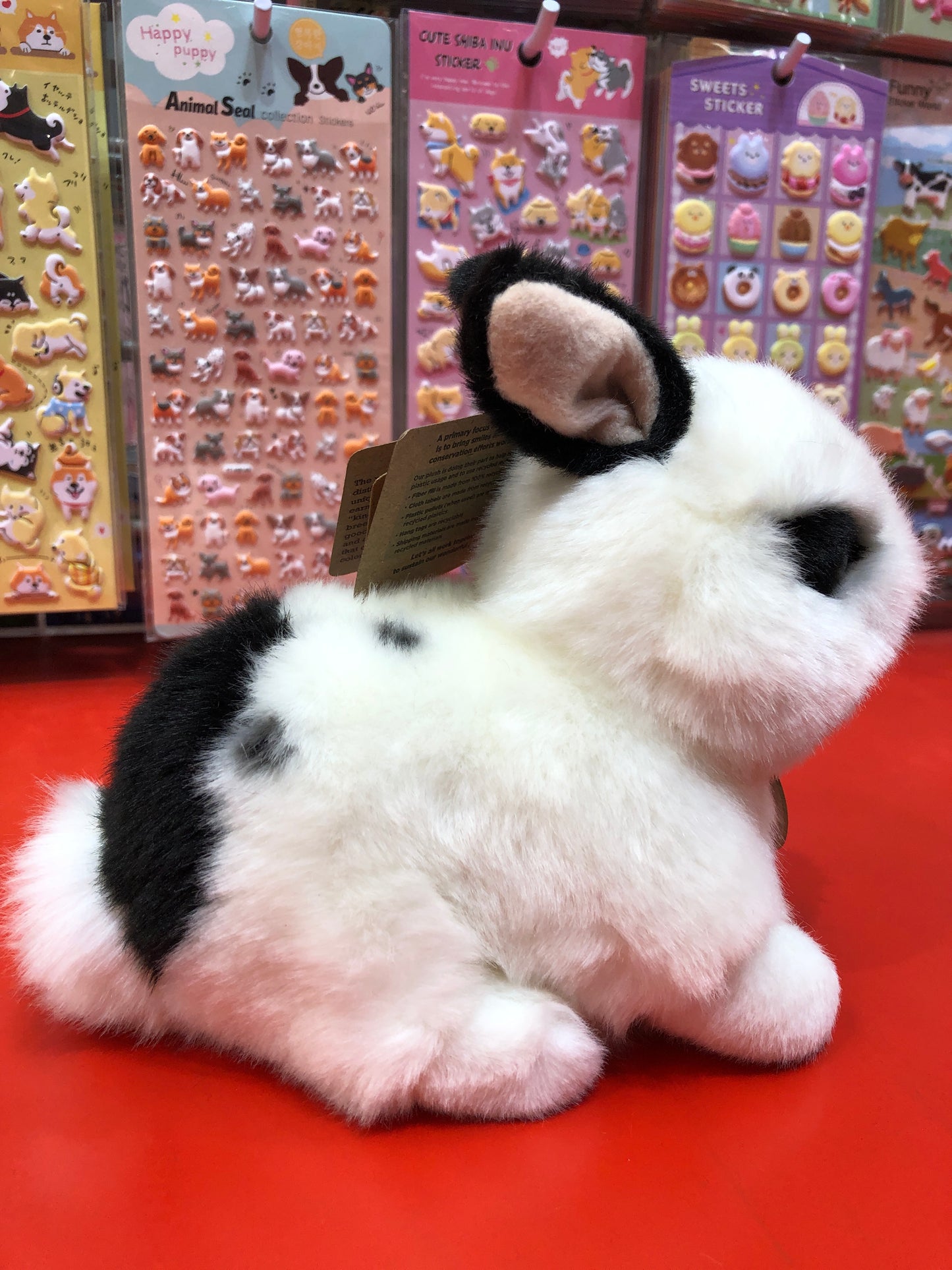 Adorable black and white Rex rabbit plush toy displayed with colorful animal sticker sheets in background