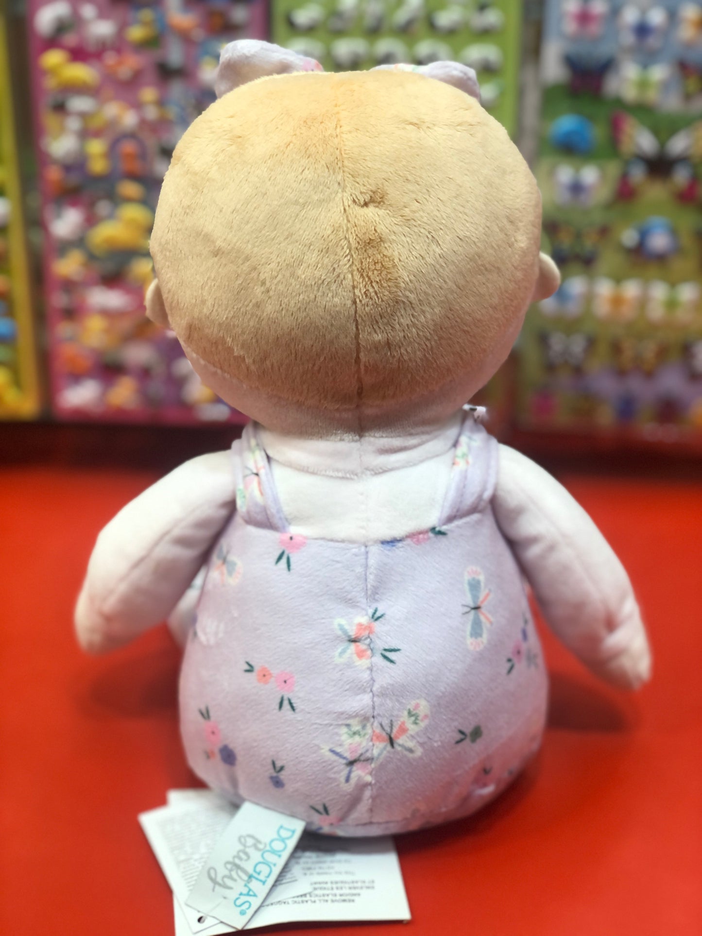 Willa Butterfly Flower plush doll with blonde hair, lavender overalls with floral pattern, shown from behind on red display shelf