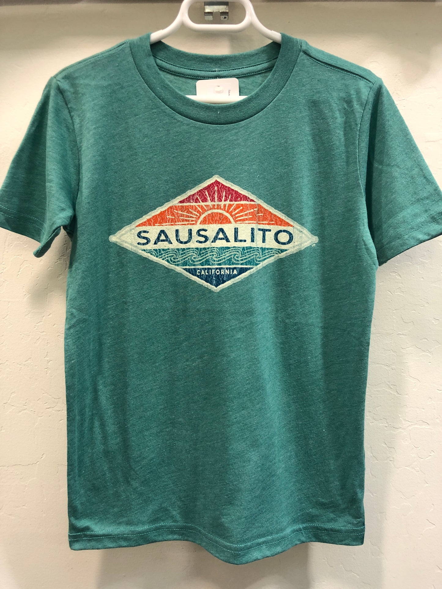 Green kids' t-shirt with Sausalito California logo featuring stylized sun and waves in diamond shape