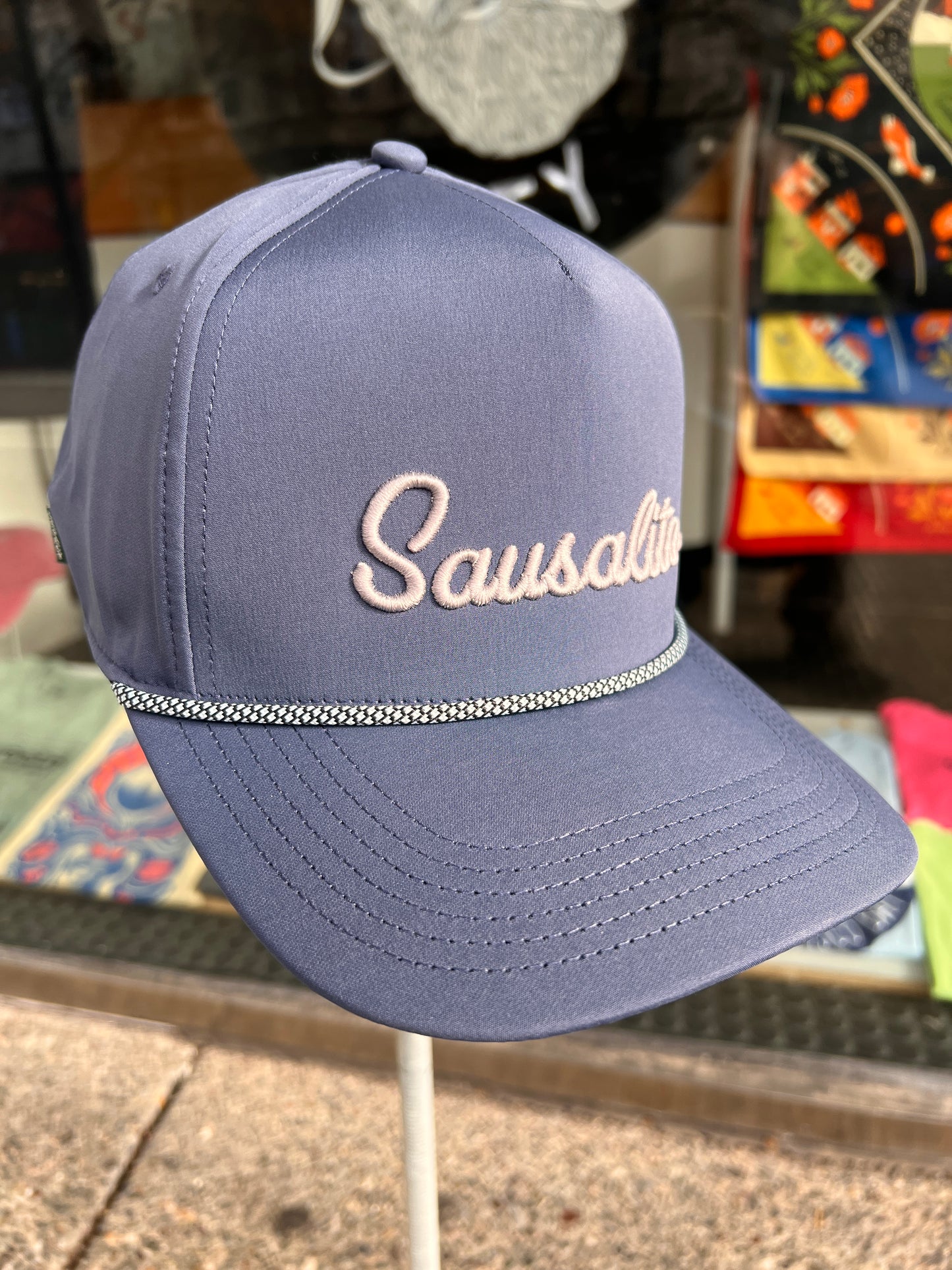 Navy blue Sausalito rope hat with grey embroidered script and decorative braid, displayed in store setting