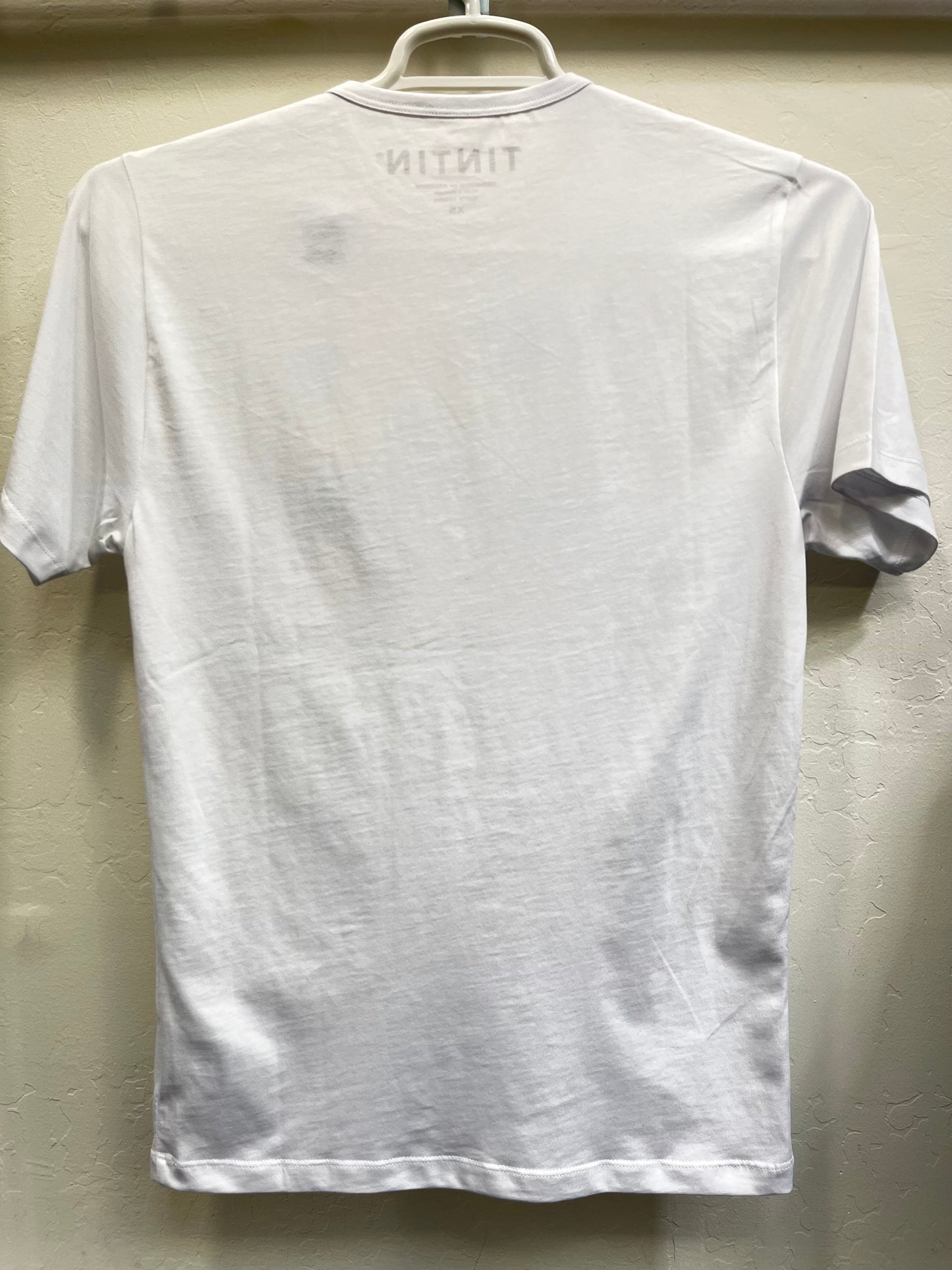 White Tintin & Co unisex t-shirt hanging on display, showing back with "TINTIN" printed at top