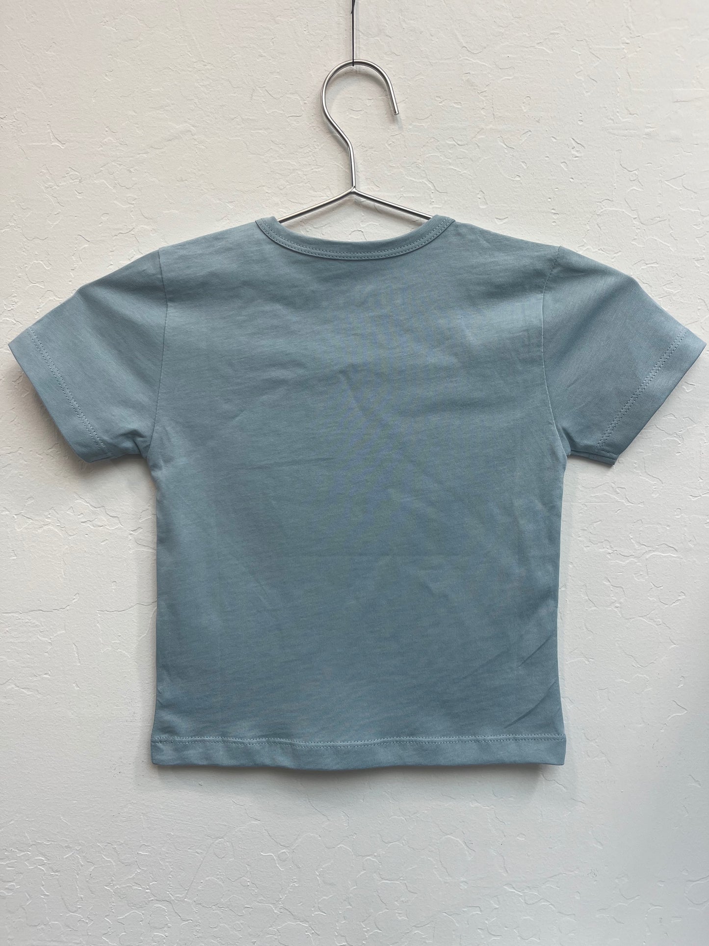 Blue kids' t-shirt with Tintin Snowy angel and devil design hanging on metal hanger against white wall