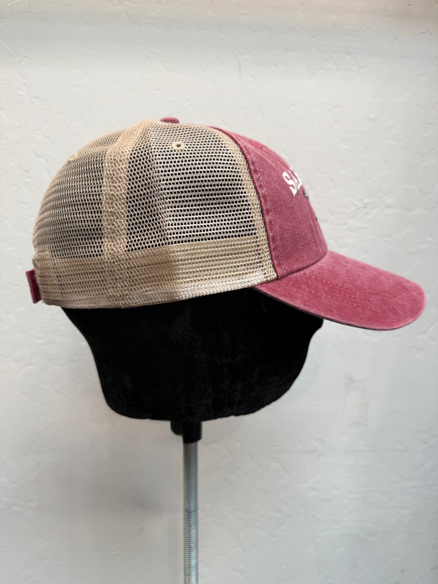 Sausalito CA trucker hat with pink washed cotton front, tan mesh back, and adjustable strap on display stand