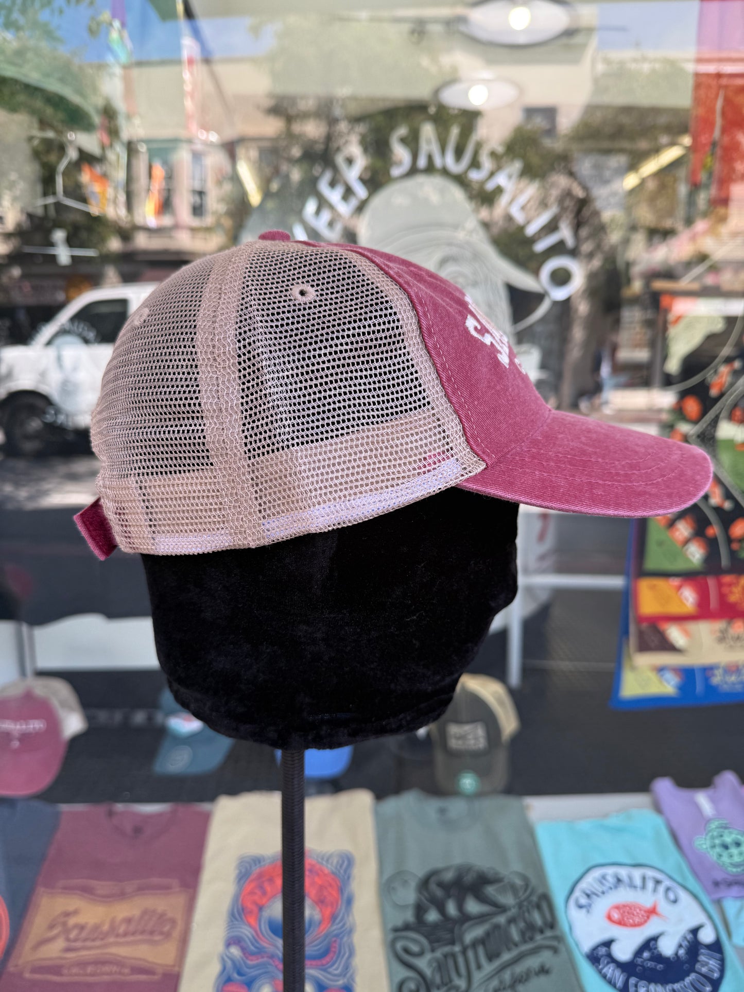 Pink and beige trucker hat on a mannequin head with a store window in the background