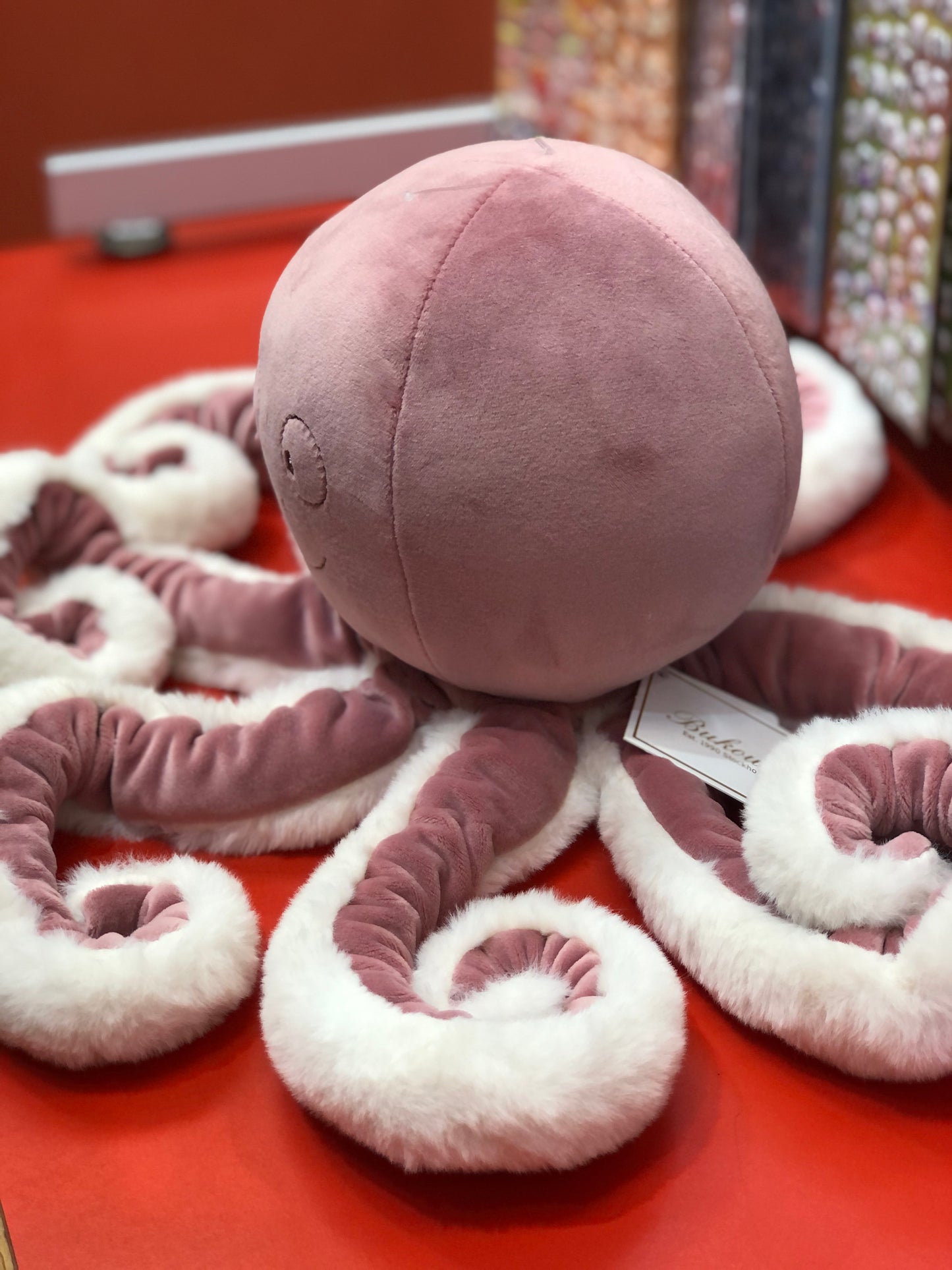 Pink plush octopus toy with soft tentacles and round body, The Great Pinky by Bukowski Bears, on red display surface