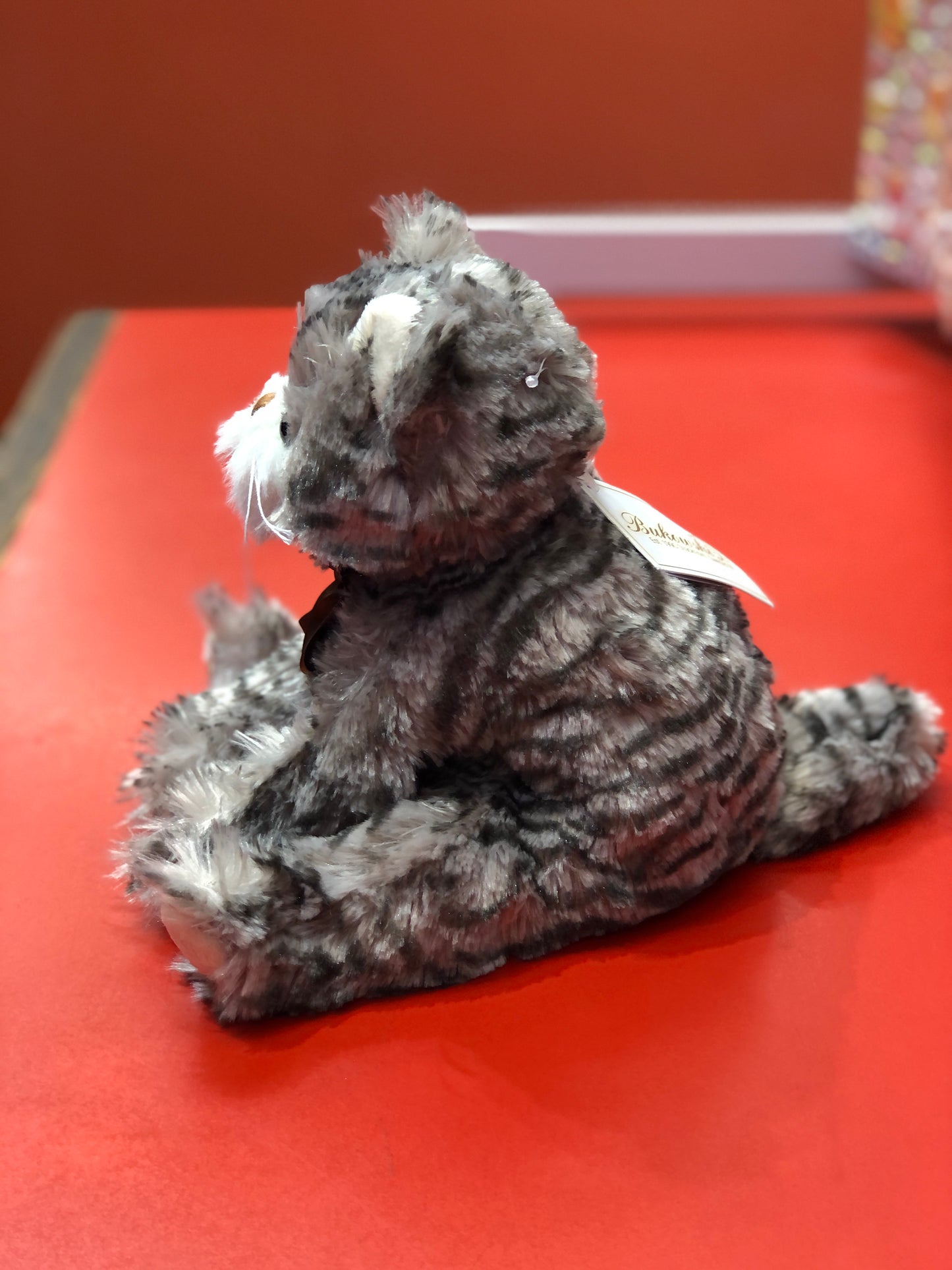 Soft gray Maciek cat plush toy from Bukowski Bears on red surface, cuddly 10-inch kitten companion for snuggling