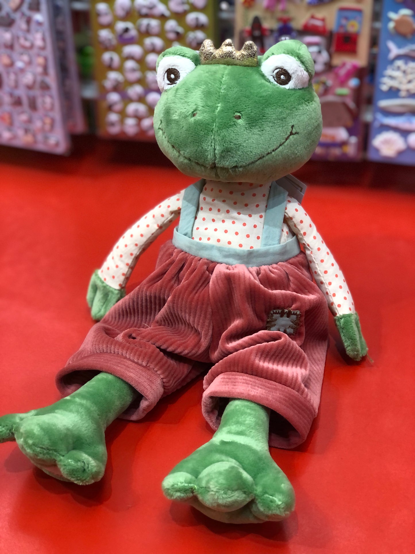 Bukowski Bears Prince Frog plush toy wearing polka-dot shirt, red overalls, and golden crown, sitting on red surface