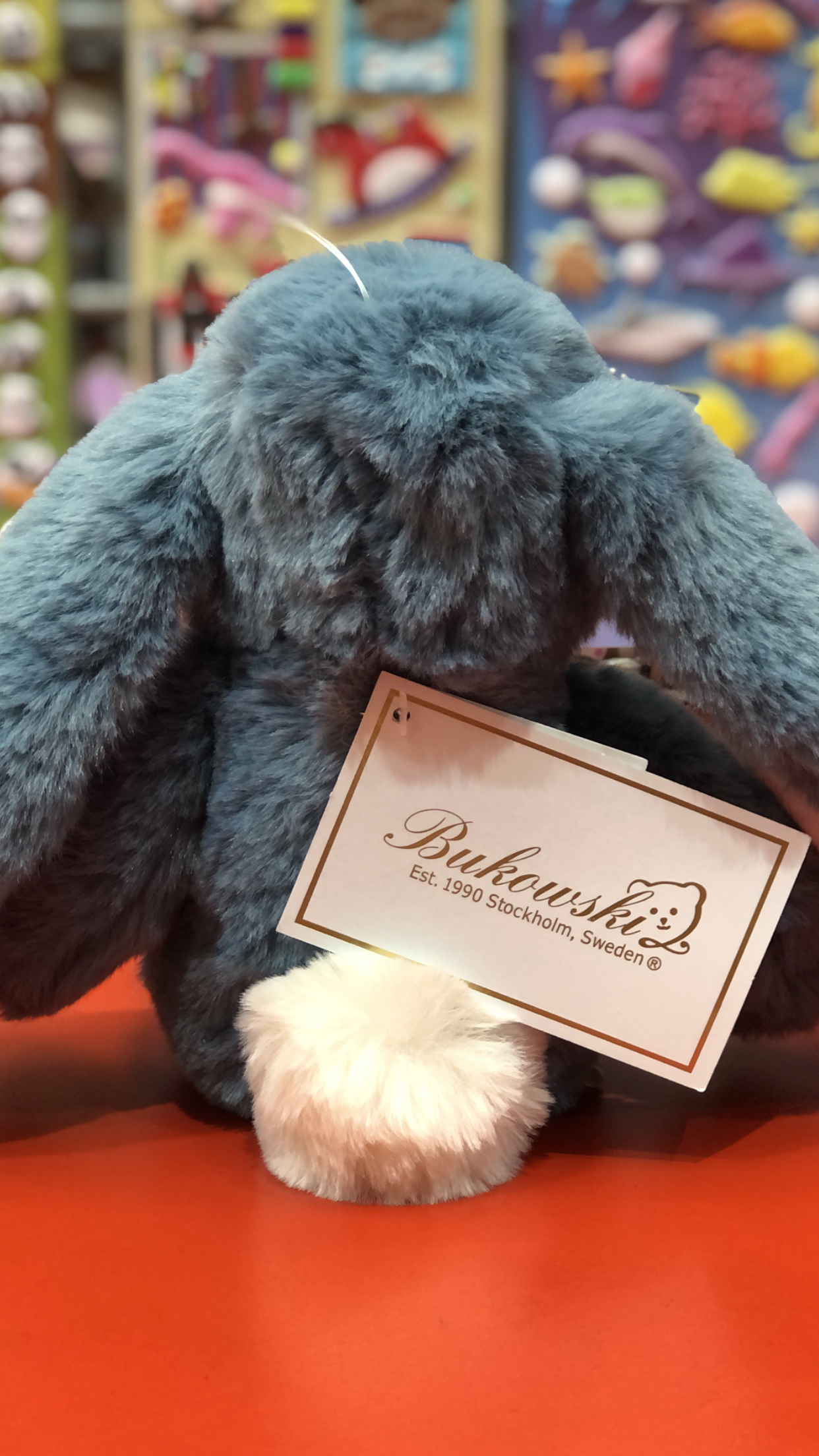 Bukowski Bears Junior Kanini plush bunny in fjord blue, with long fuzzy ears and white tail, displayed with brand tag in toy store