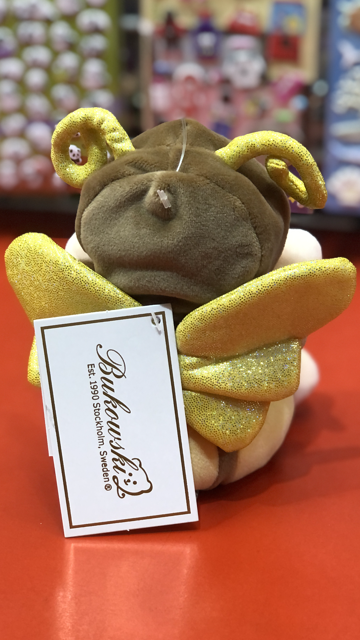 Bukowski Bears Ziggy Butterfly Lemon plush toy with yellow sparkly wings and antennae, showcasing brand tag on red surface
