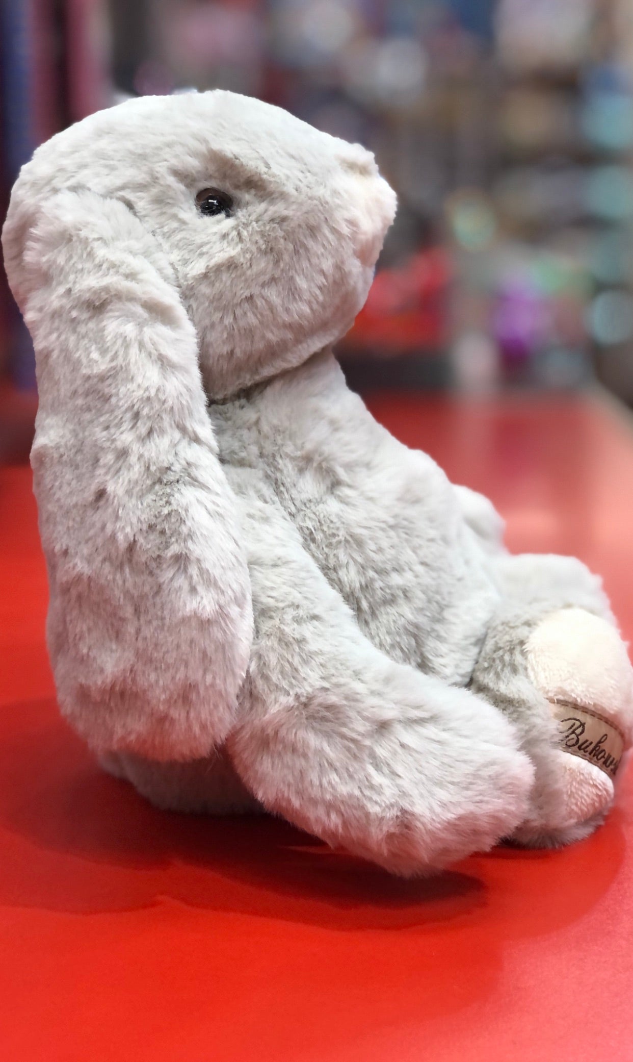 Bukowski Bears Lovely Kanini light grey bunny plush toy with long ears, sitting on red surface, perfect for cuddling