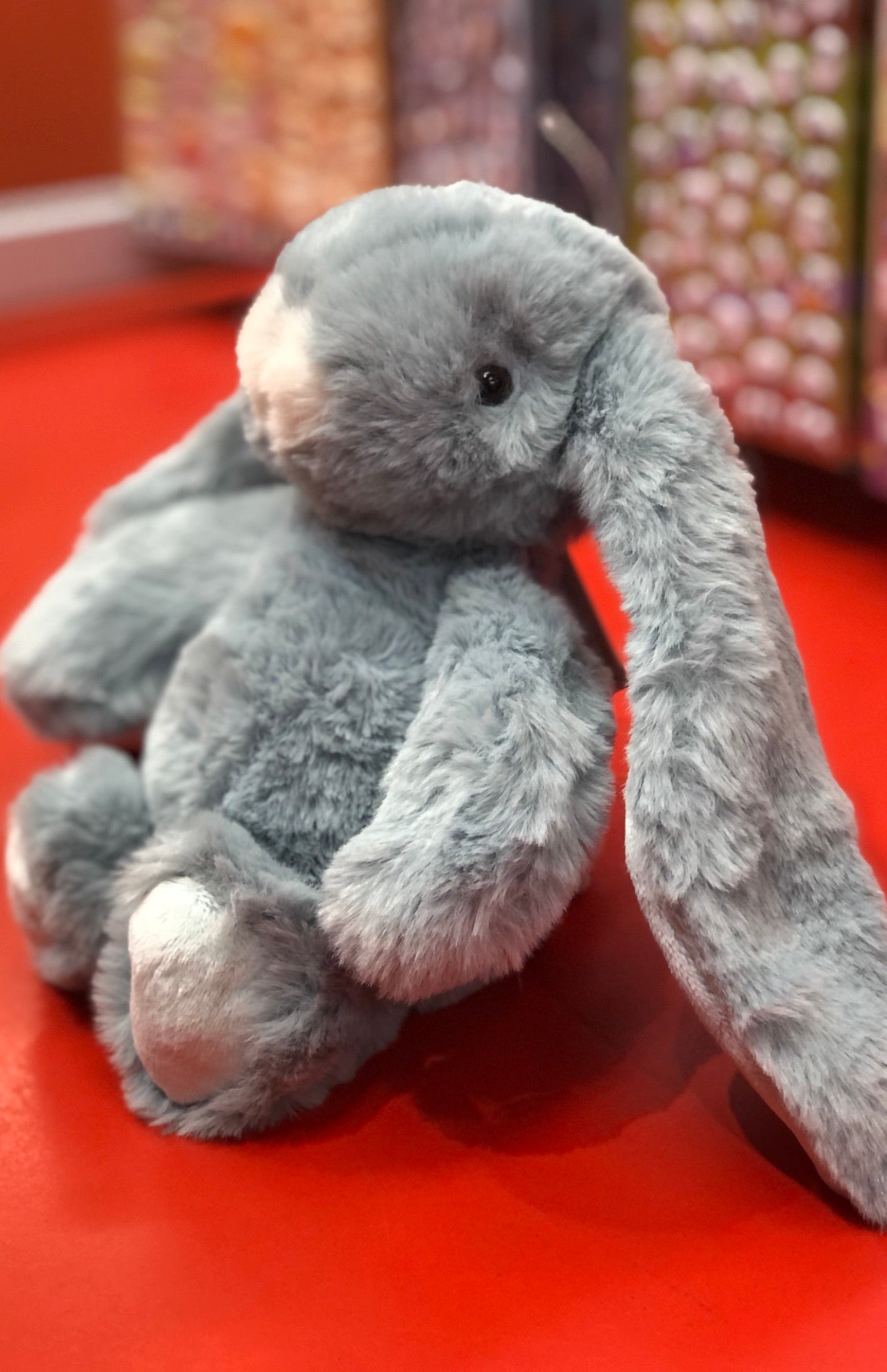 Soft blue bunny plush with extra-long ears on red surface, perfect bedtime companion for babies and toddlers