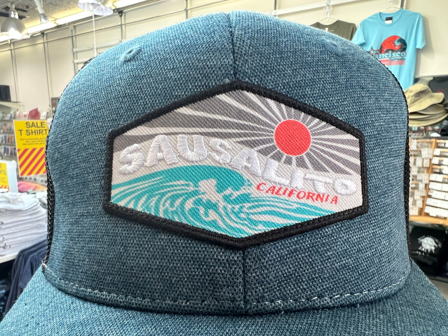 Sausalito trucker cap with embroidered patch featuring sun, waves, and California text on teal mesh-back hat