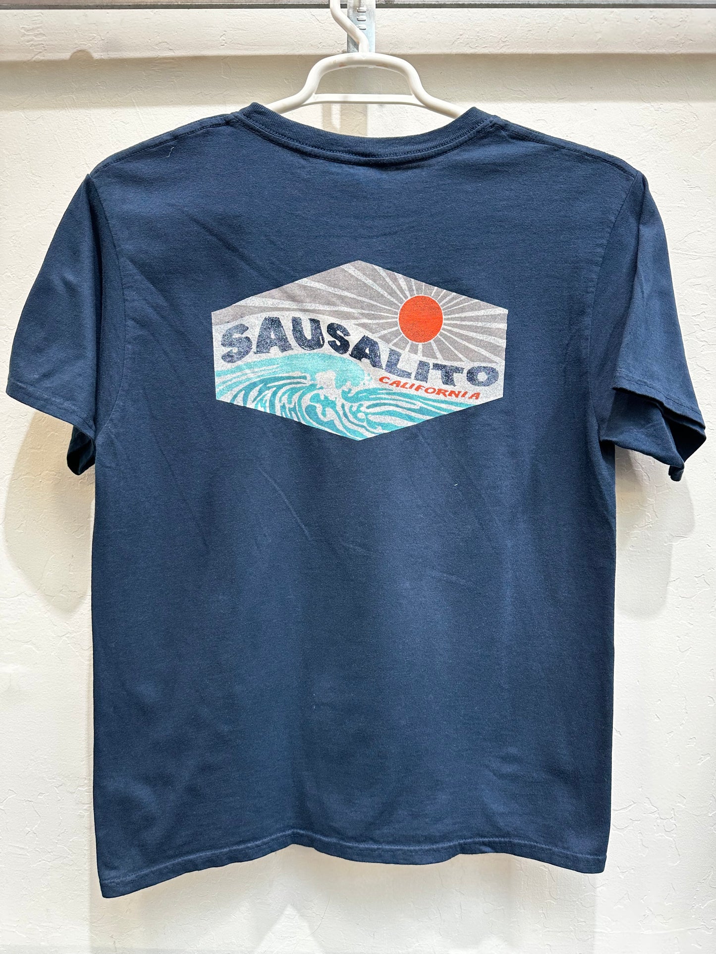 Navy Affirmation Wave t-shirt with Sausalito California graphic featuring waves and sun, hanging on white hanger