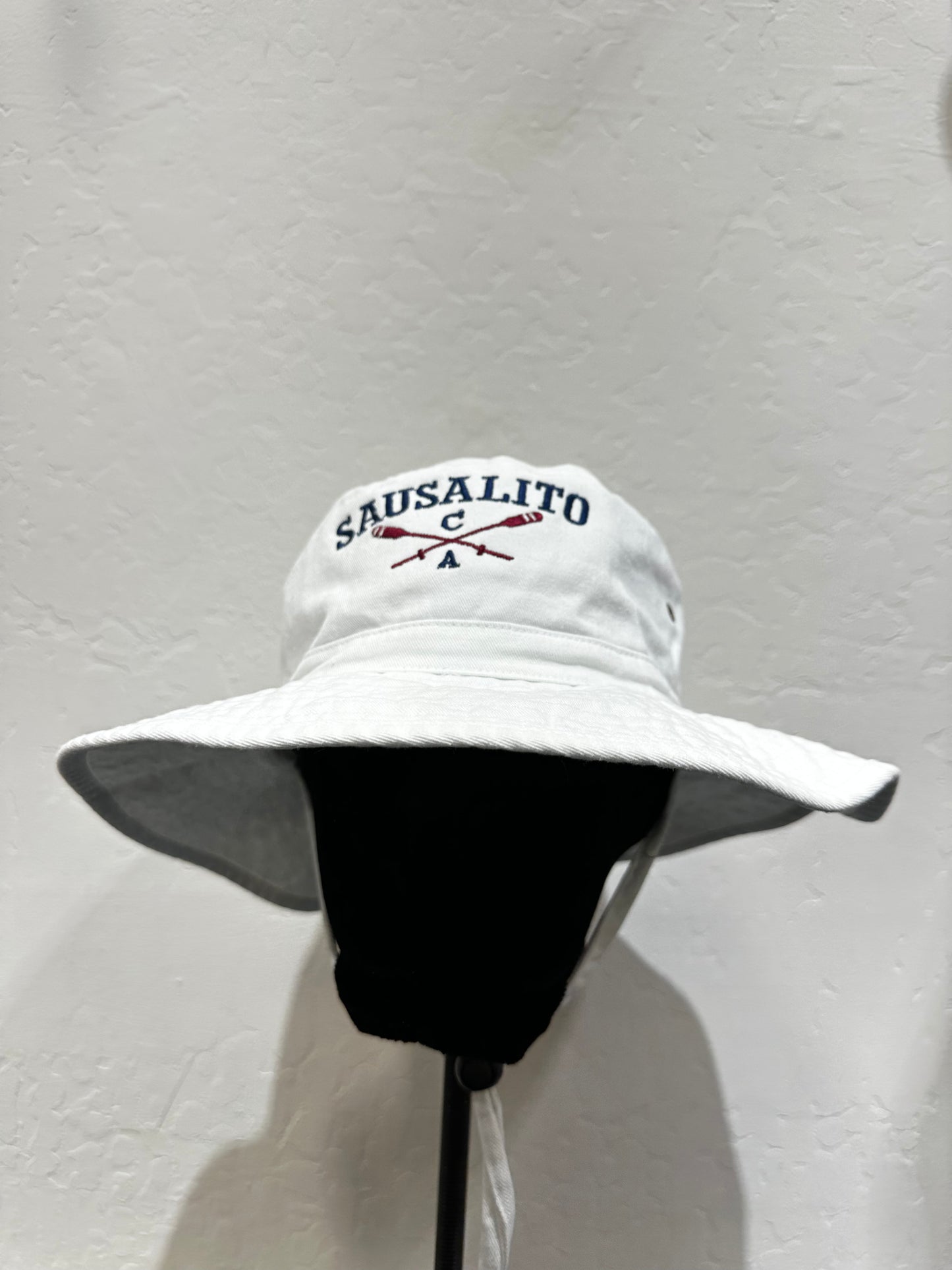 White cotton bucket hat with Sausalito logo and crossed oars, wide brim, displayed on stand against light background