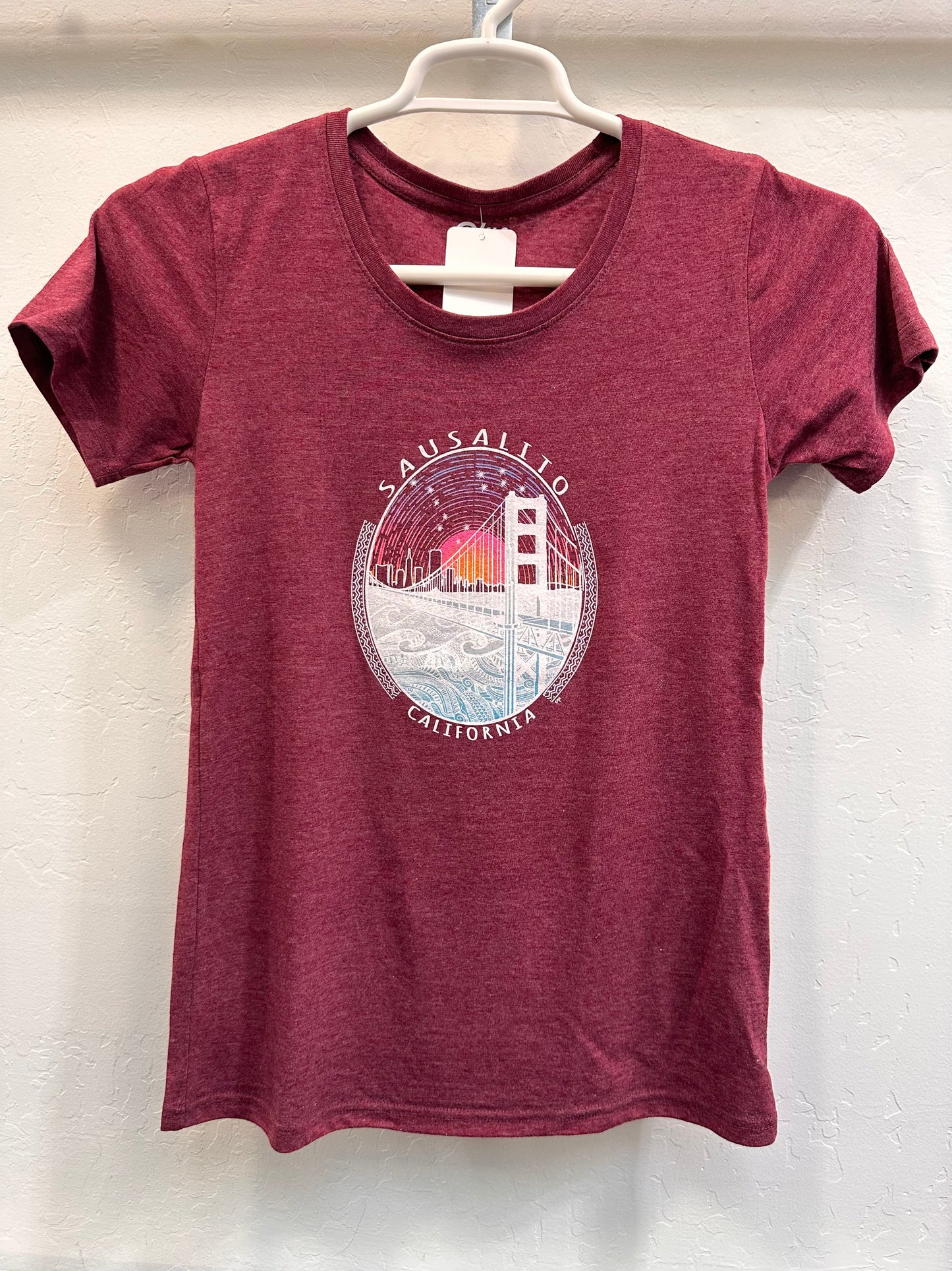 Sausalito Golden Gate Bridge women's t-shirt with sunrise design, maroon color, hanging on display