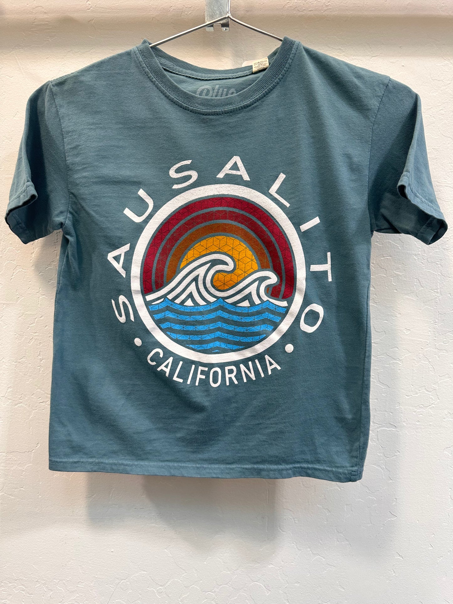 Sausalito California kids' t-shirt with colorful wave design and sunset graphic, hanging on display