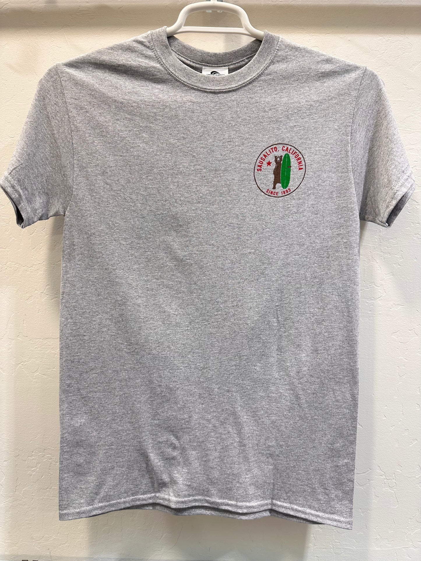 Gray t-shirt with Sausalito California logo featuring surfing grizzly bear, hanging on white hanger