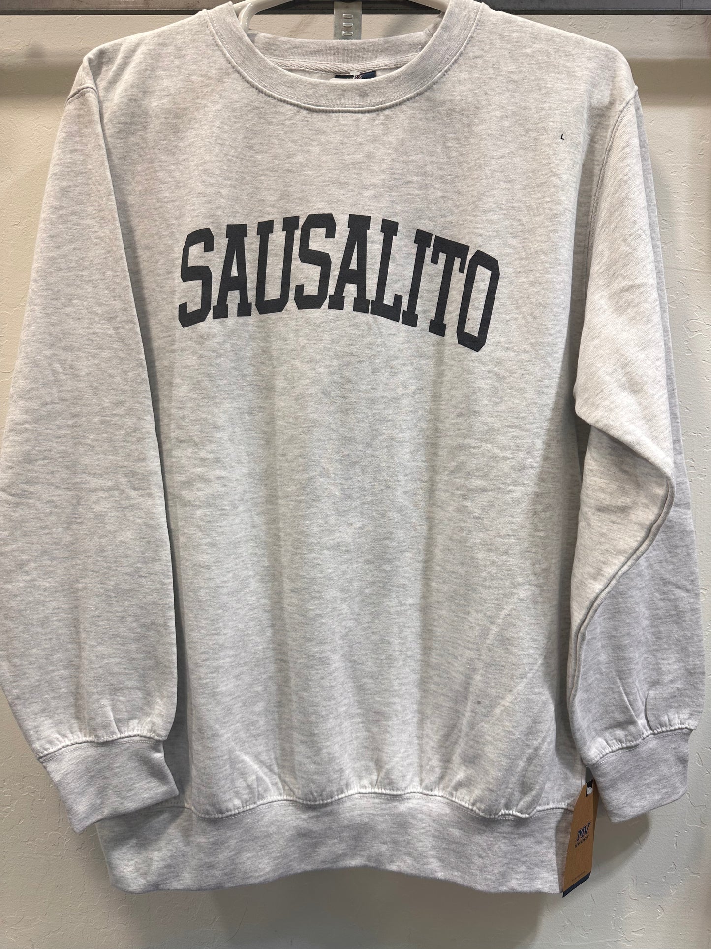 Heather grey crewneck sweatshirt with "SAUSALITO" boldly printed in black, hanging on display