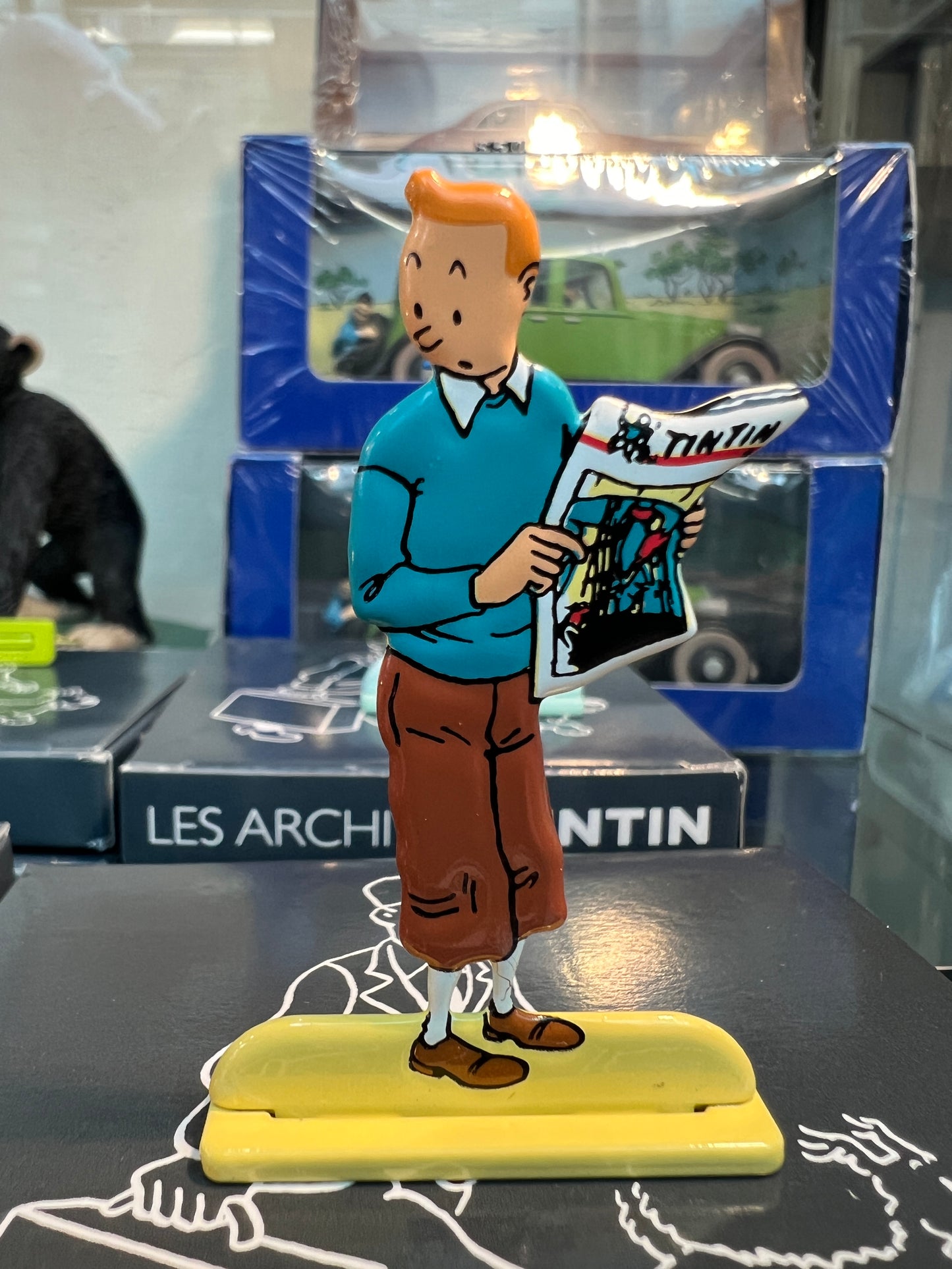 Tintin metal figure holding newspaper, displayed with Les Archives Tintin book and collectible boxes, vintage comic collectible