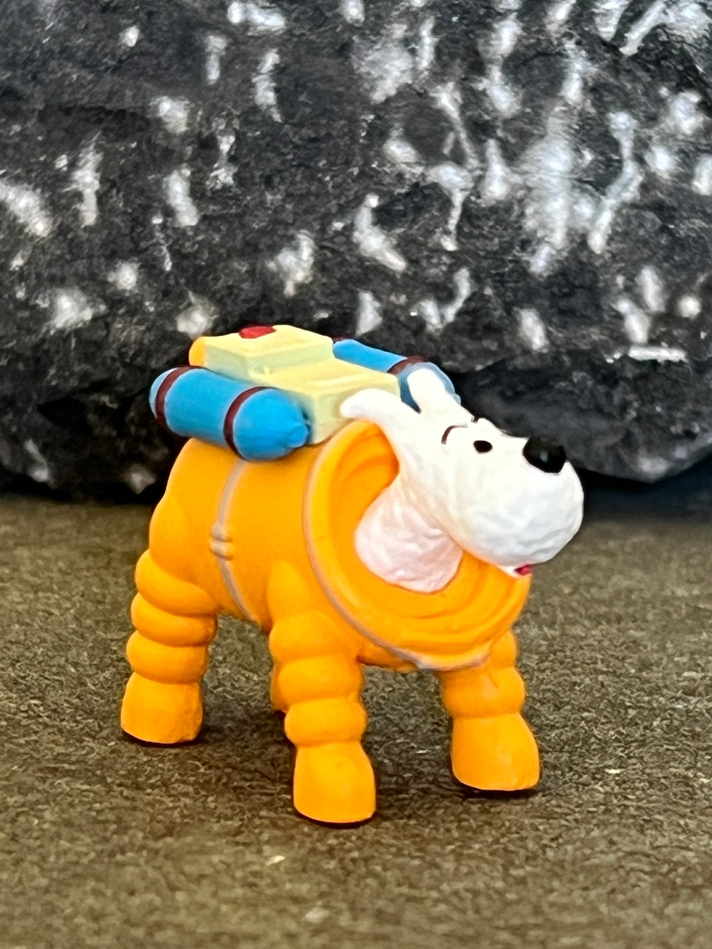 Tintin's dog Milou figurine in orange space suit from Adventures on the Moon, with blue oxygen tank on rocky background