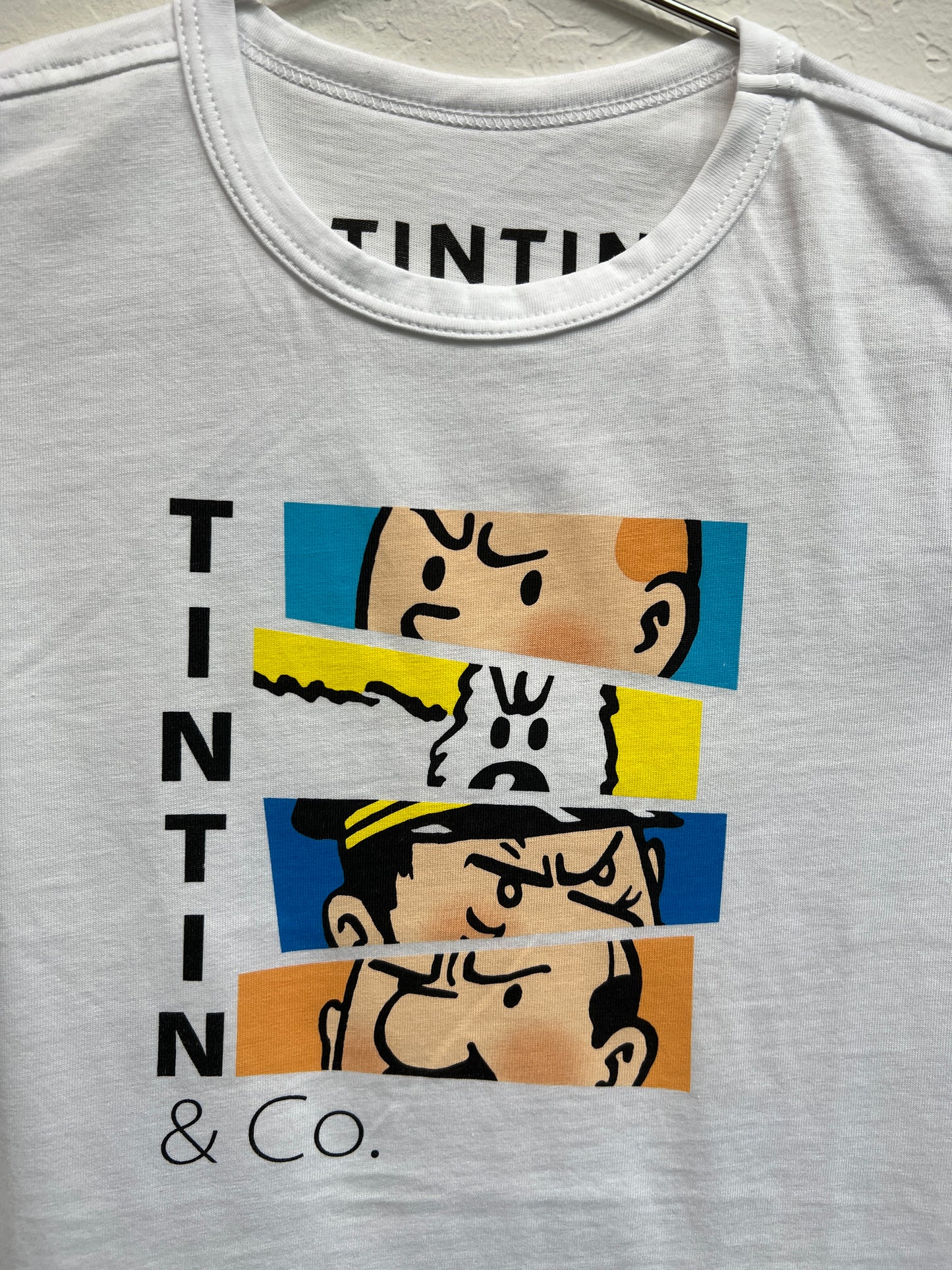 Tintin & Co kids' t-shirt featuring colorful character faces, including Tintin, Snowy, and others, on white cotton fabric