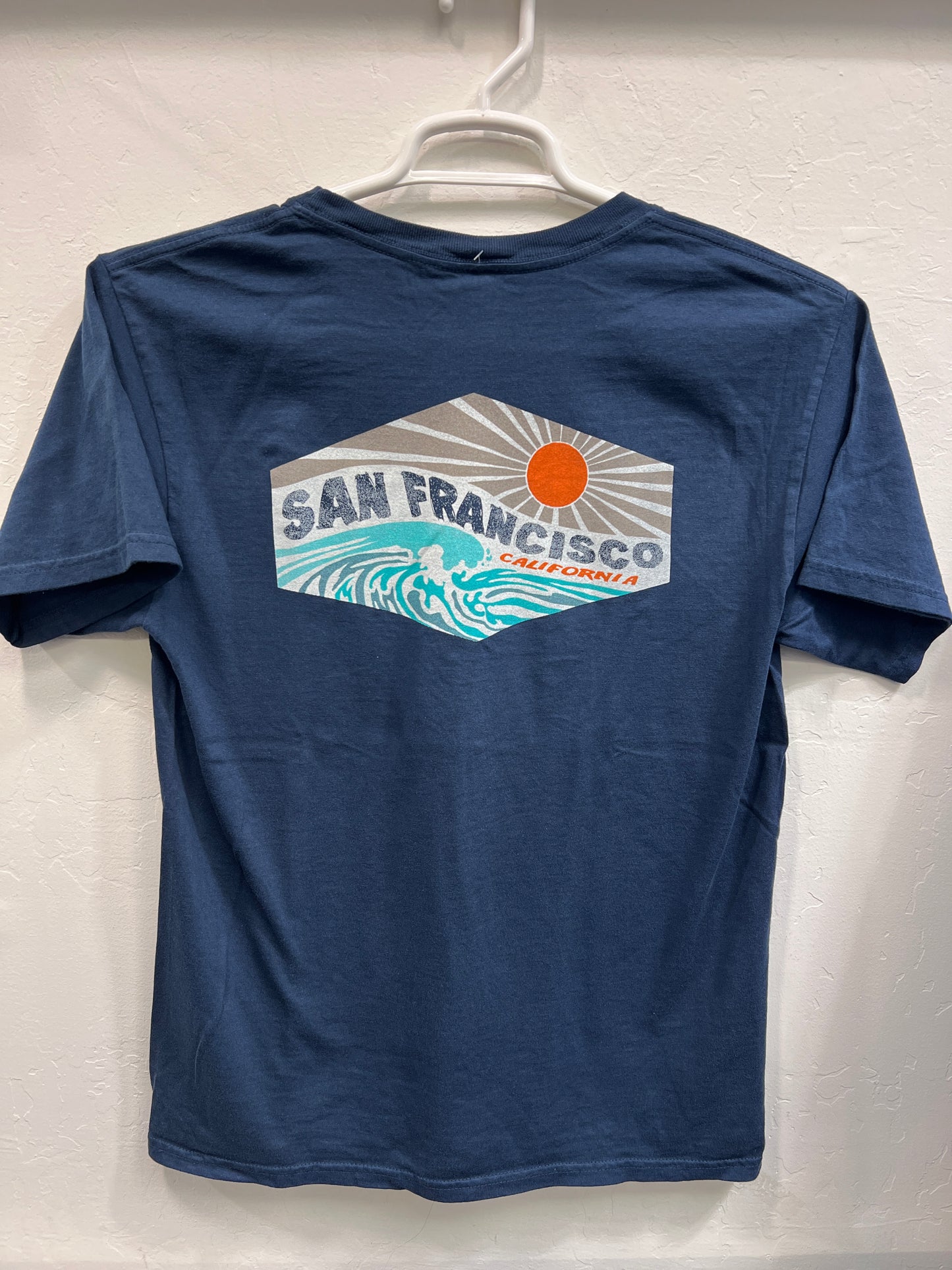 Navy Affirmation Wave t-shirt with San Francisco California design featuring ocean waves and sun, hanging on display