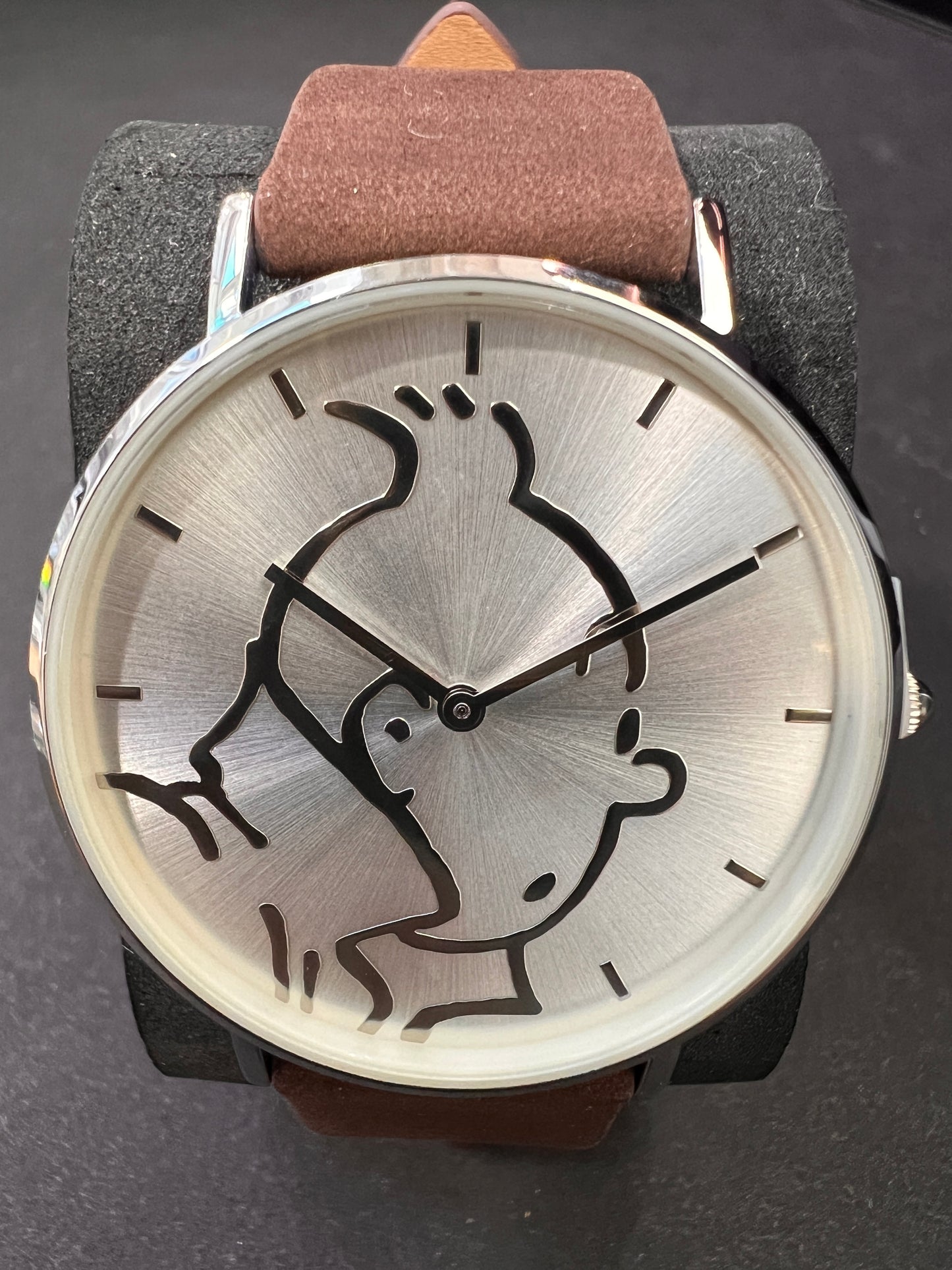 Tintin watch with classic character silhouette on silver face, brown leather strap, metal case, displaying adventurous spirit