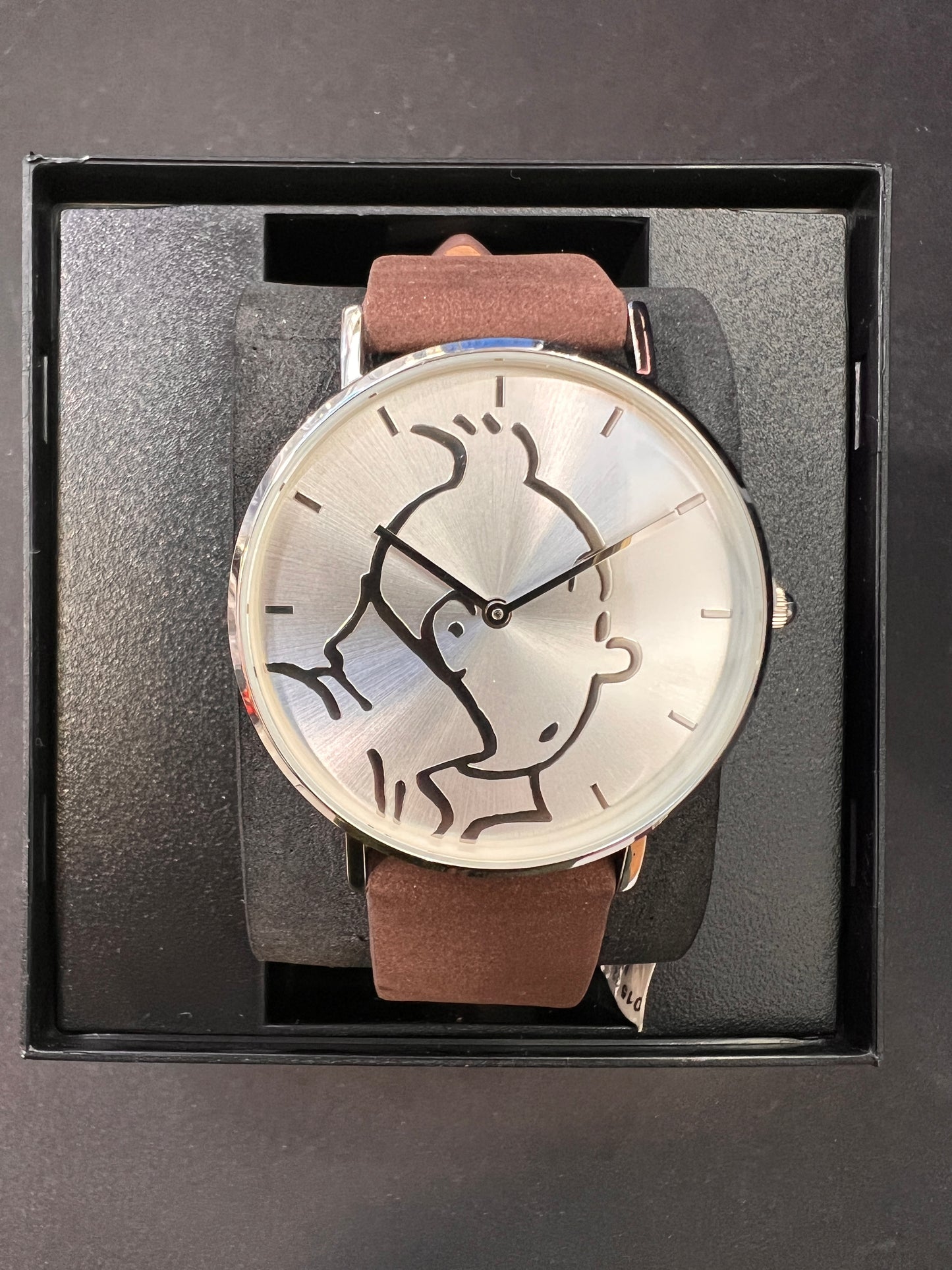 Tintin watch with brown leather strap, silver face featuring character outline, displayed in black box