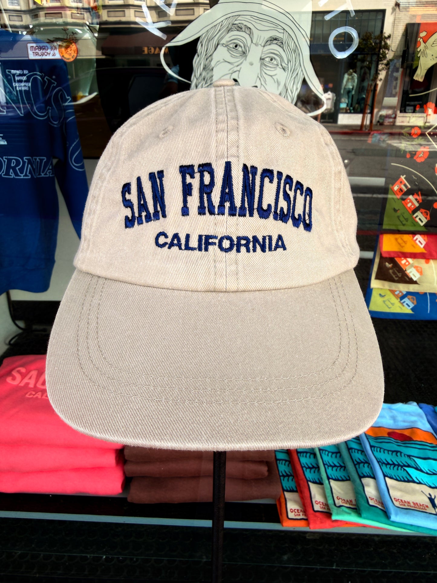 Front view of a khaki beige washed cotton baseball cap featuring "San Francisco" embroidered across the front in a bold navy blue arched font, with "California" stitched directly underneath.
