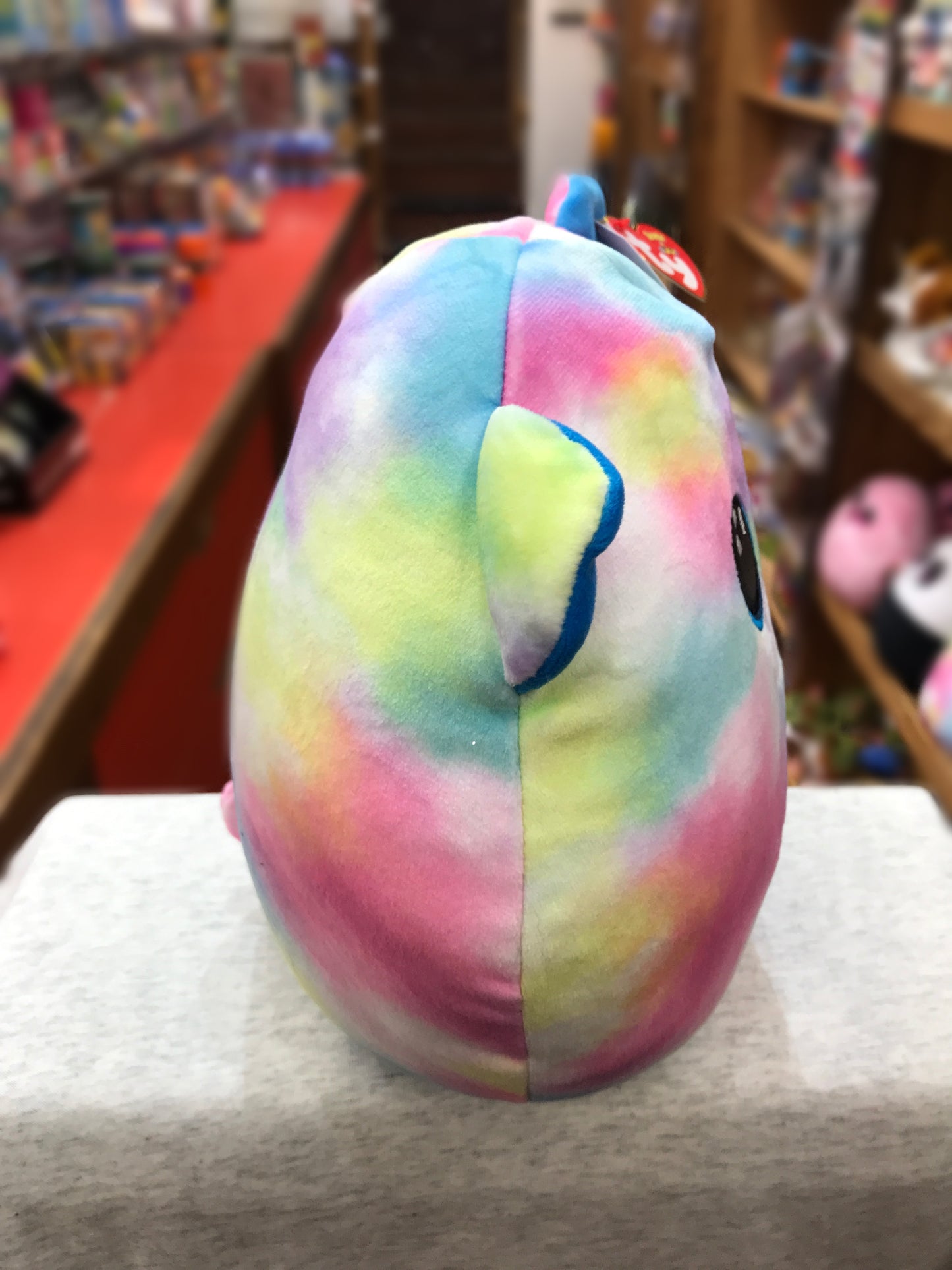 Colorful pastel Ty Squish-a-Boo Hope bear plush with blue ears, displayed in toy store setting