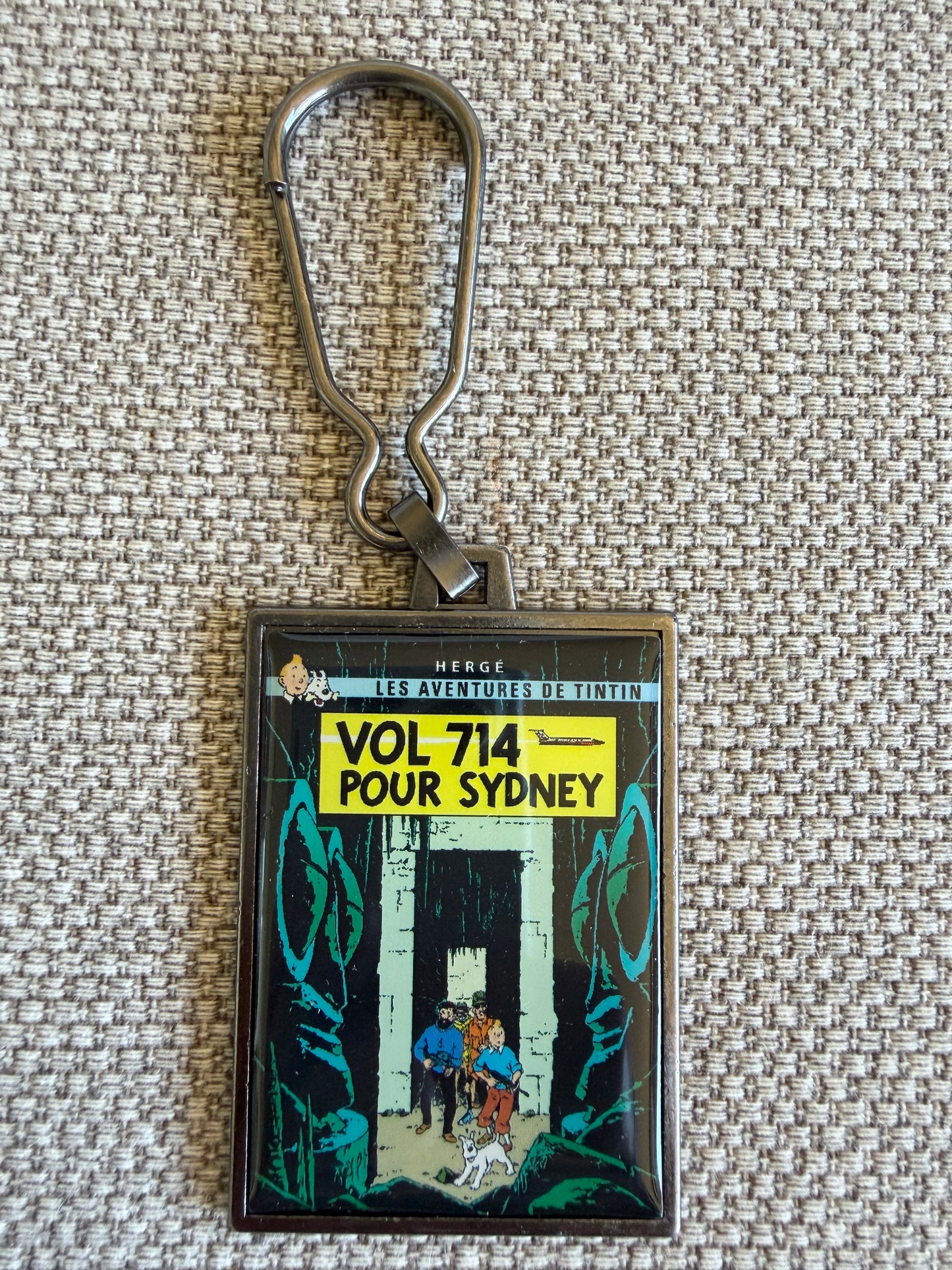 Front view of the rectangular Tintin Flight 714 to Sydney metal keychain, featuring a resin-coated replica of the original French book cover showing Tintin, Captain Haddock, and Snowy wading through a dense jungle.