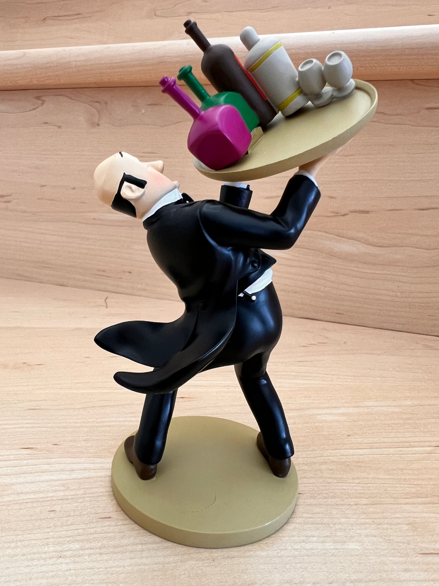 Rear view of the Nestor resin figurine from "The Castafiore Emerald," showing the back of his black tuxedo coat tail flying out to the side as he balances on one foot on a round, tan base.