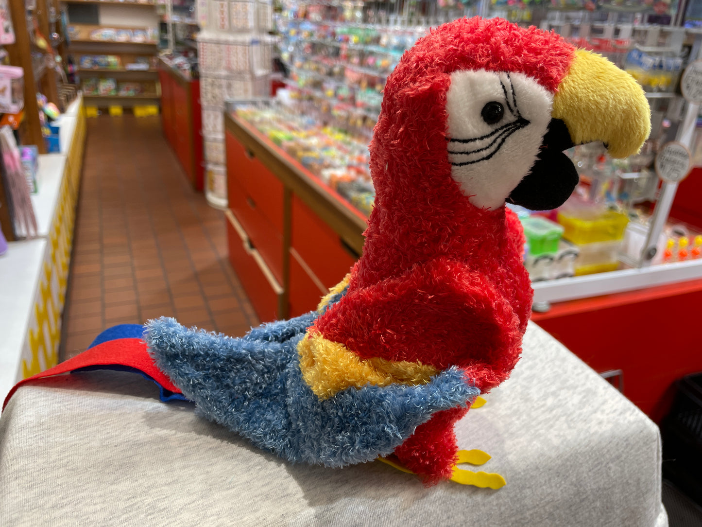 Colorful Gabby the Parrot plush toy with red, blue, and yellow feathers displayed in a toy store aisle