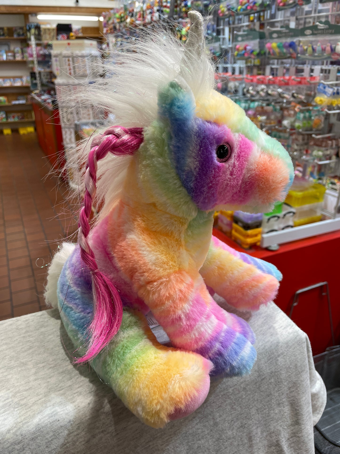 Colorful rainbow unicorn plush toy with sparkly mane and horn, displayed in toy store setting