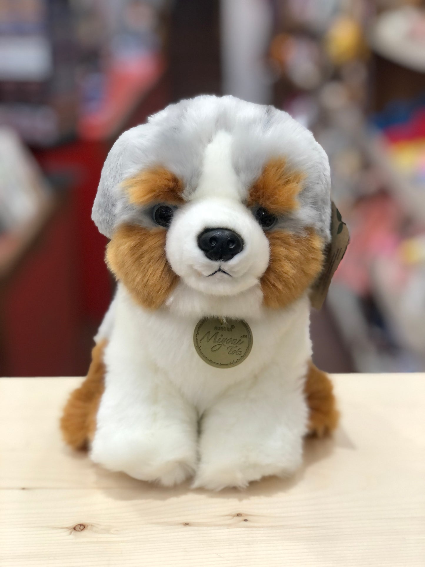 Adorable Miyoni Tots Australian Shepherd plush puppy with realistic mixed-color coat and expressive face, sitting on wooden surface