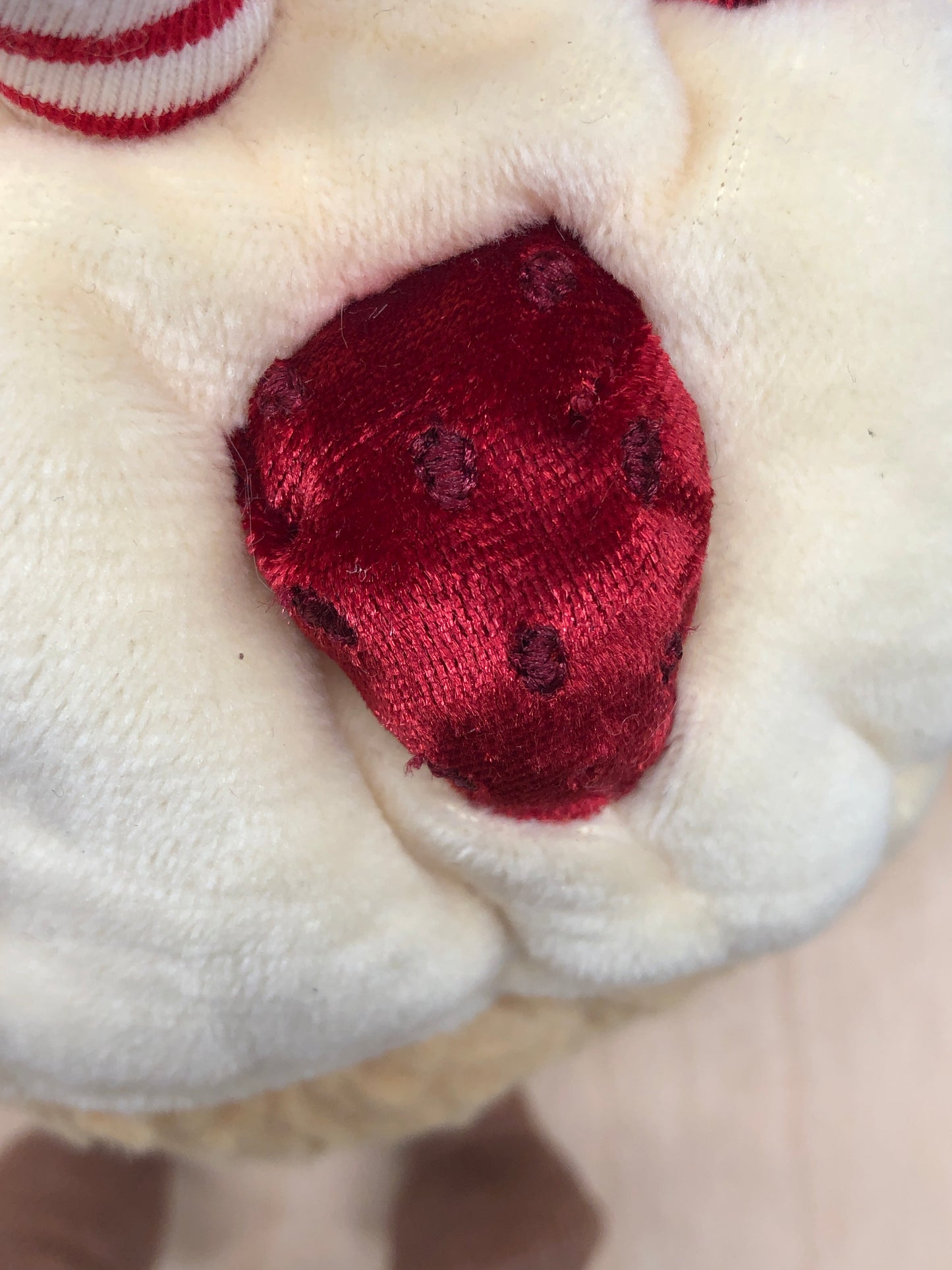 Close-up of Jellycat Amuseables Birthday Cake plush, showing soft cream fur and velvety red strawberry detail