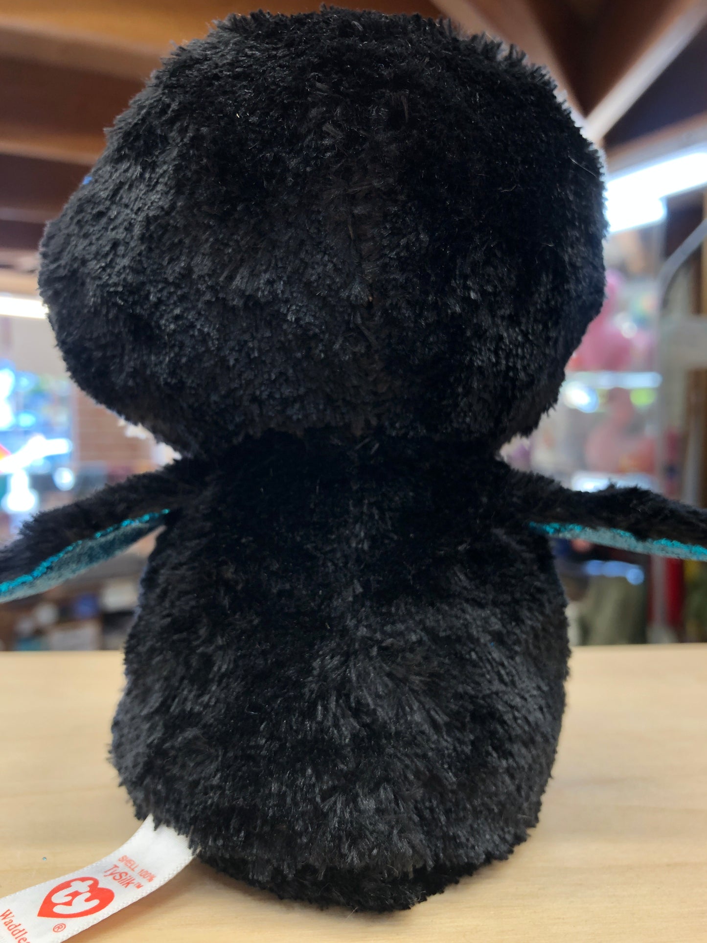 Plush black Ty Beanie Boo Waddles penguin toy, rear view showing soft fluffy texture and Ty tag on shelf in store