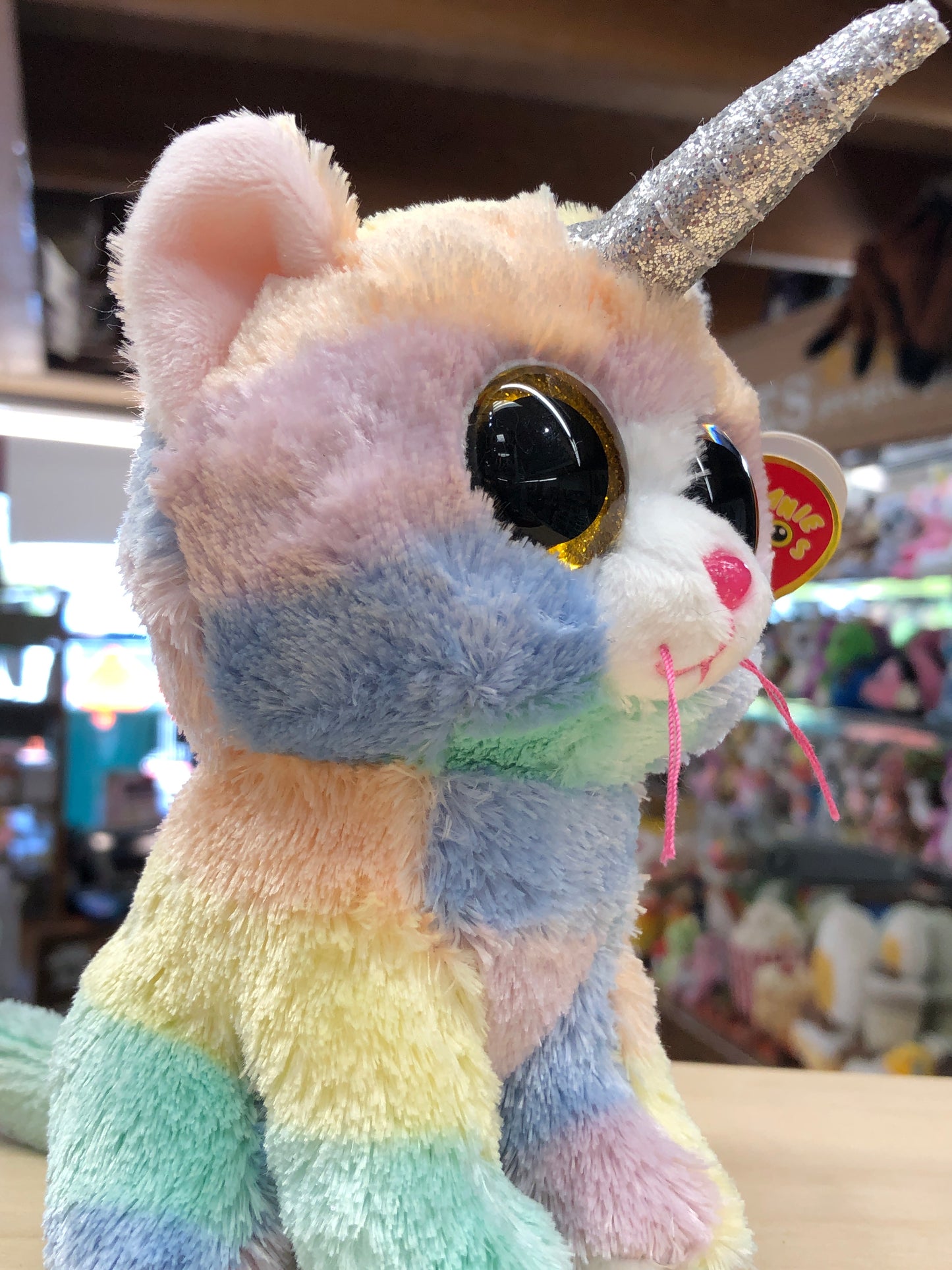 Pastel rainbow Ty Beanie Boo unicorn cat plush with glittery silver horn and large sparkly eyes, displayed in toy store