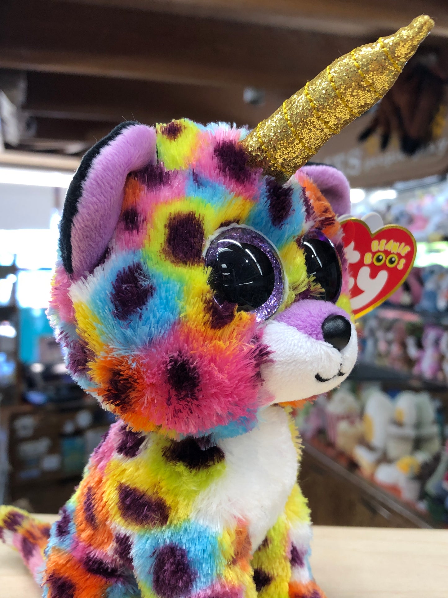 Colorful Ty Beanie Boo unicorn plush with gold horn and sparkly eyes, displayed in toy store with tag visible