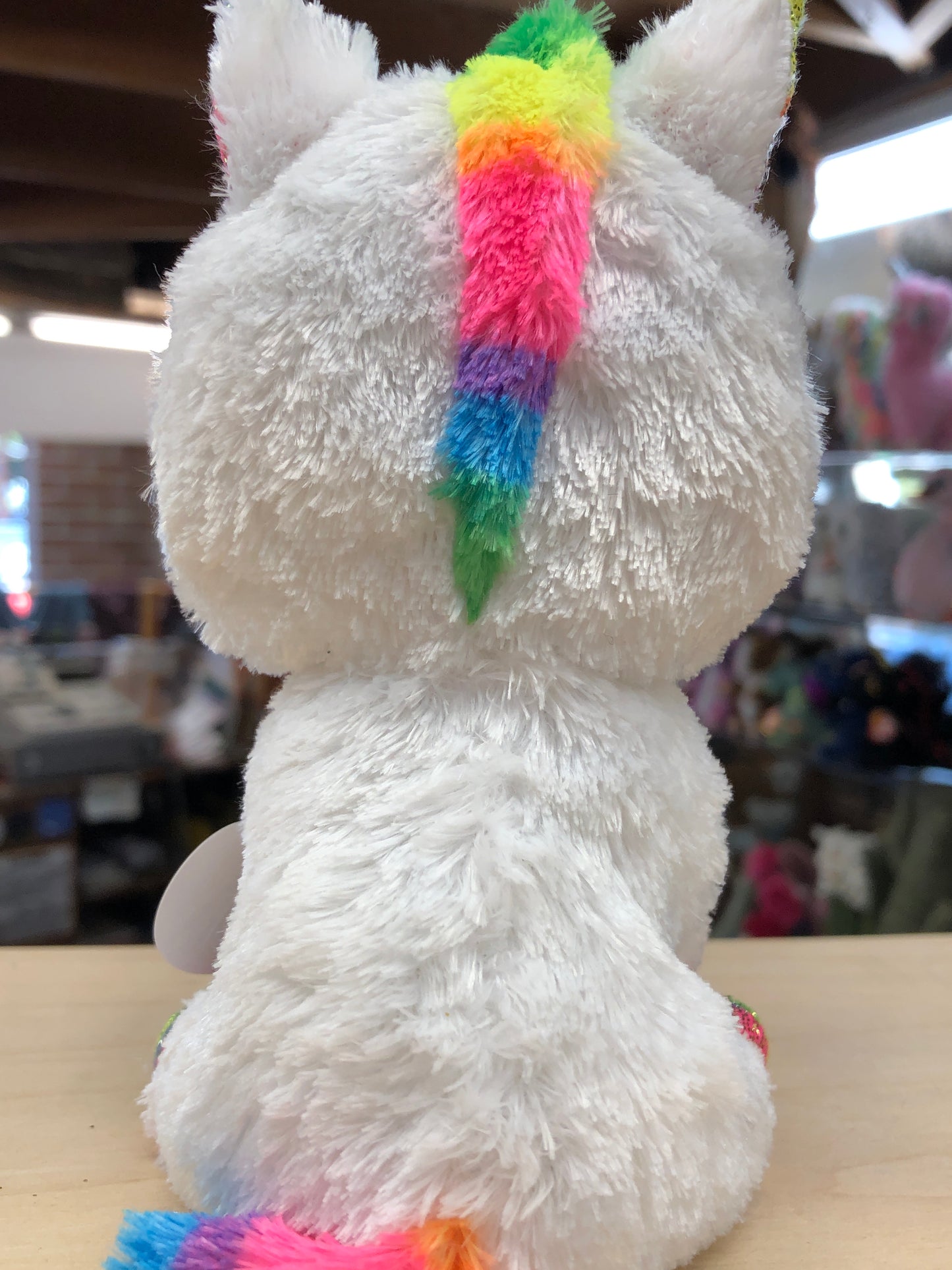 Ty Beanie Boo Pixy unicorn plush with rainbow horn and tail, white fuzzy body, sitting on display table