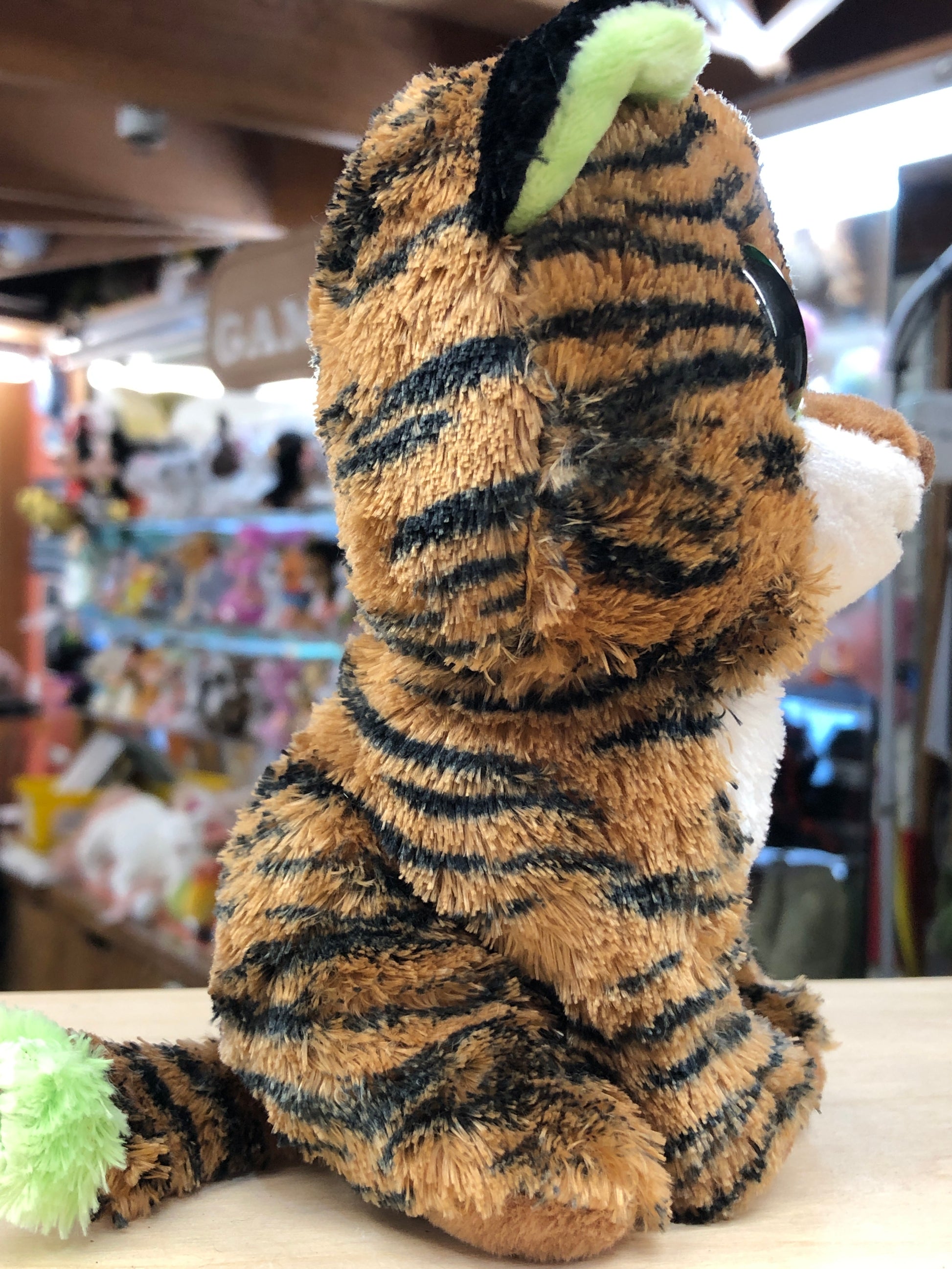 Ty Beanie Boo Tiggy plush tiger with brown fur, black stripes, and unique green ears, sitting on display in a toy store