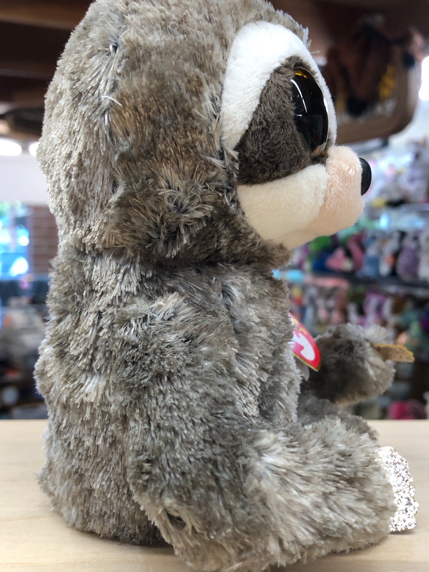 Ty Beanie Boo Dangler sloth plush toy with large eyes, soft gray fur, and white face markings, displayed in store