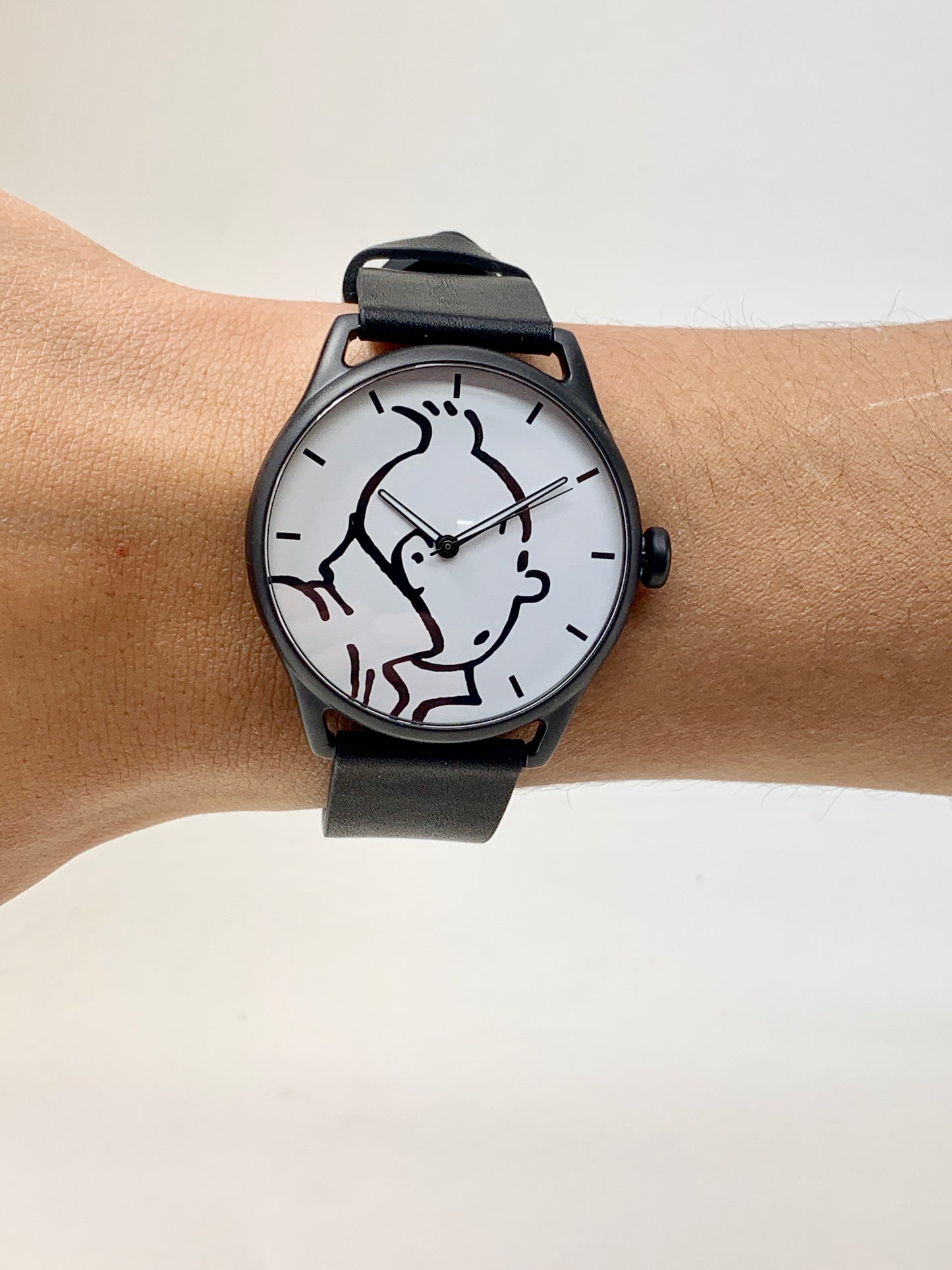 Tintin watch with black and white character design on white face, black case and leather strap, worn on wrist
