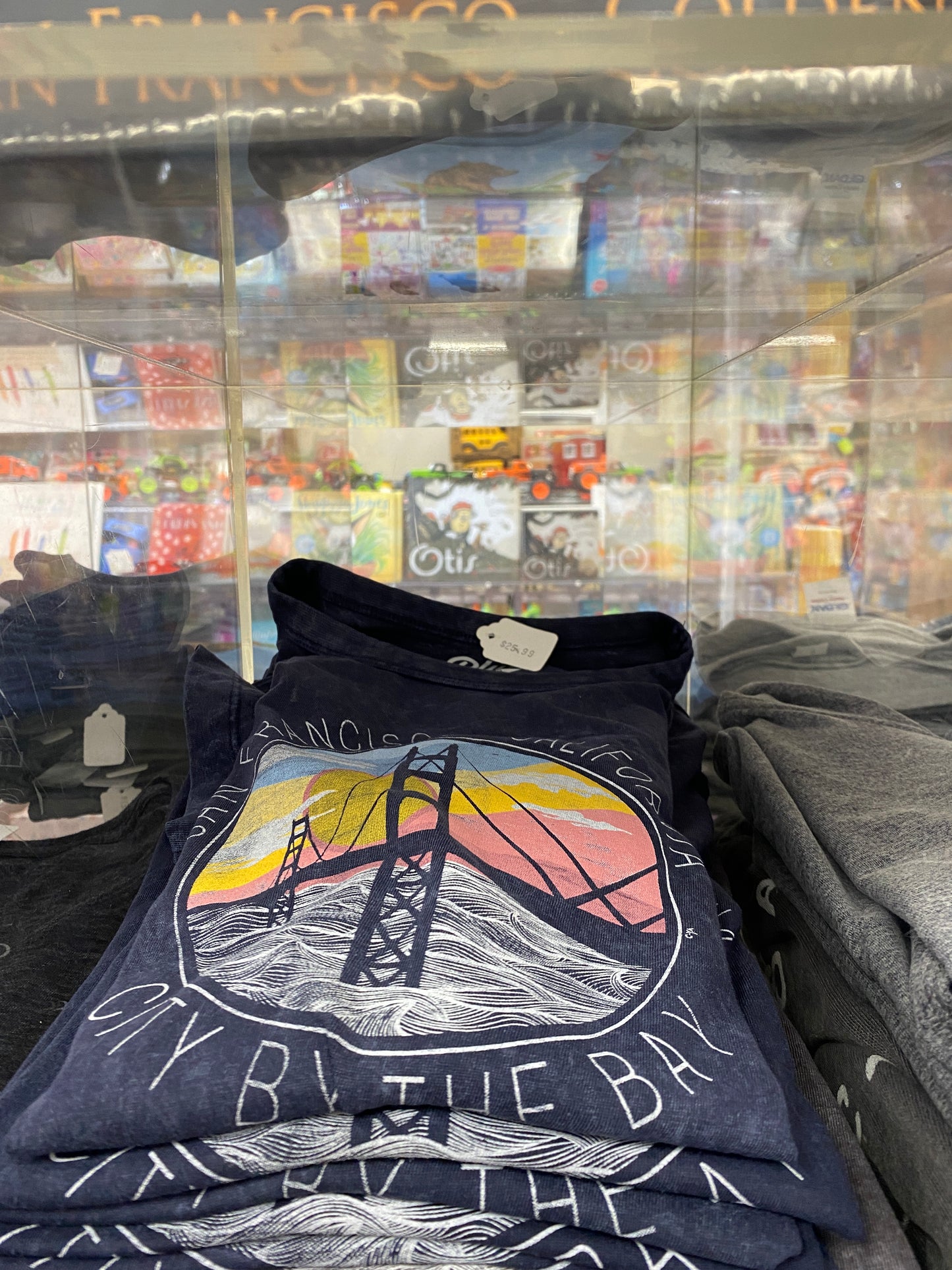 San Francisco Golden Gate Bridge t-shirt with sunset design in souvenir shop display, surrounded by other merchandise
