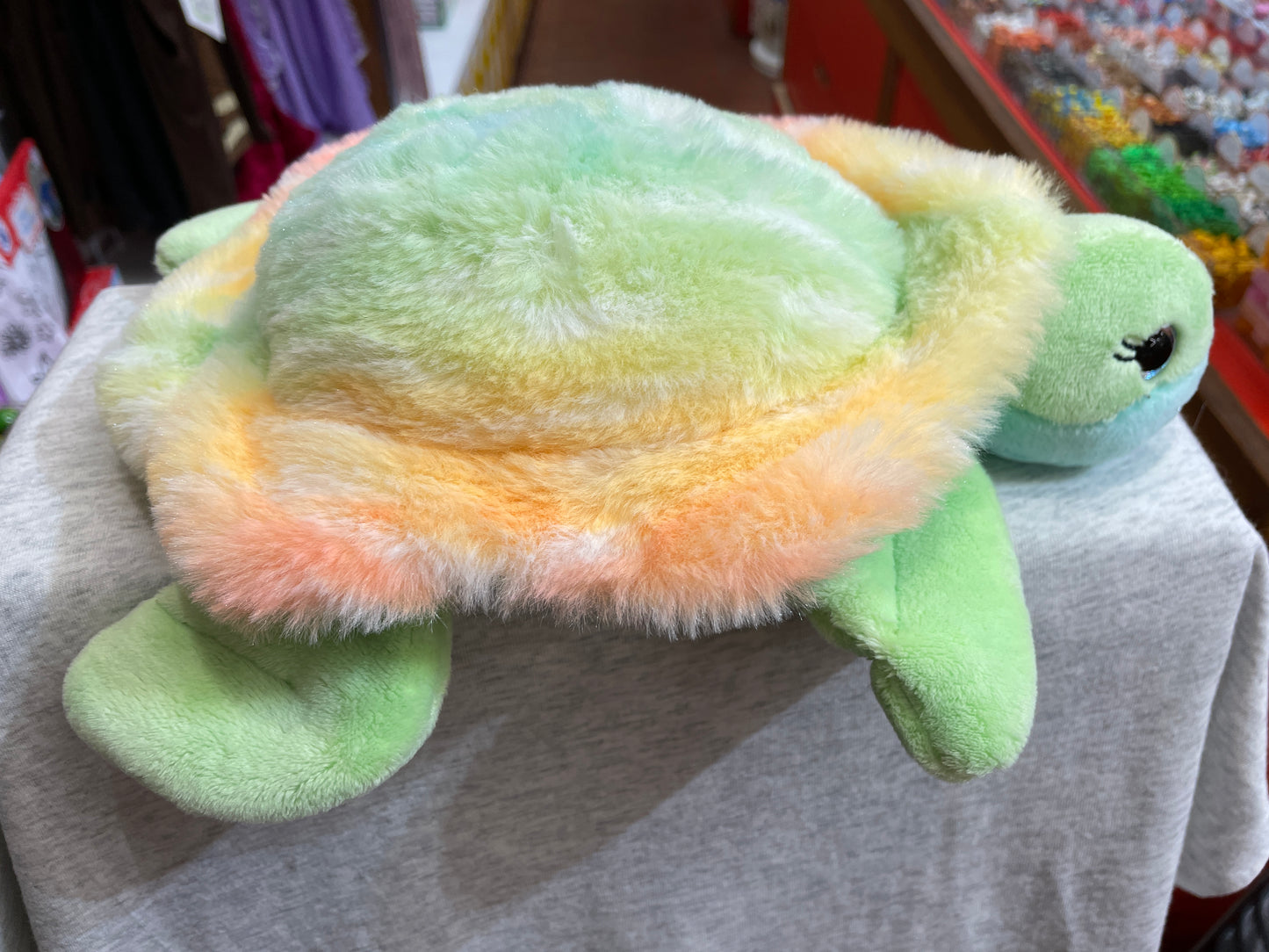 Colorful plush sea turtle toy with rainbow shell, green flippers, and blue eyes, perfect for cuddling and ocean-themed adventures