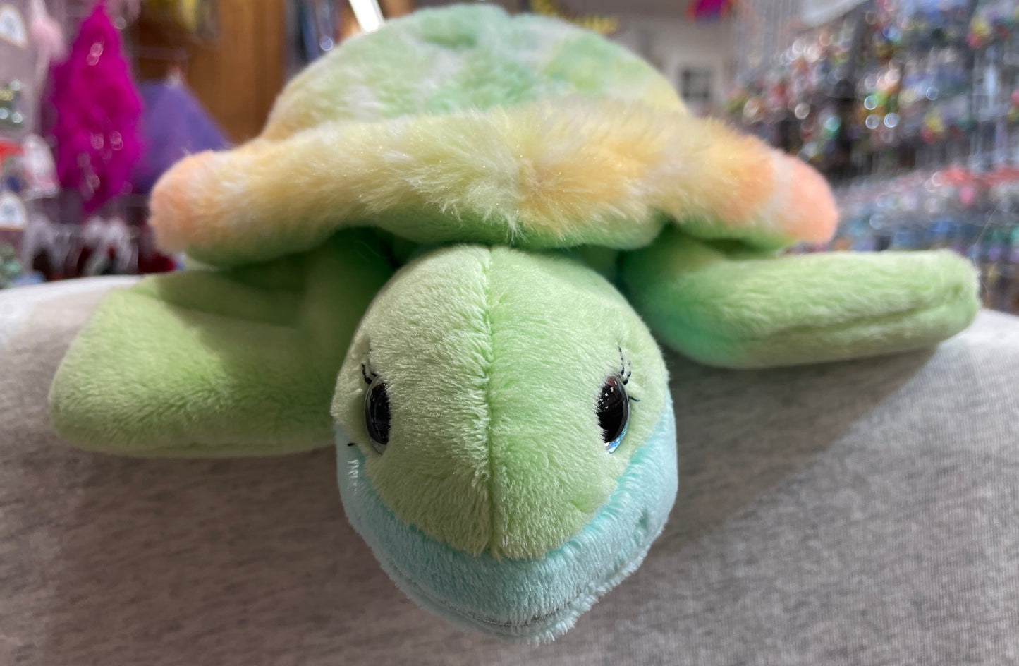 Colorful plush sea turtle Nyla with rainbow shell, green body, and sparkling blue eyes, perfect for cuddling and nautical adventures