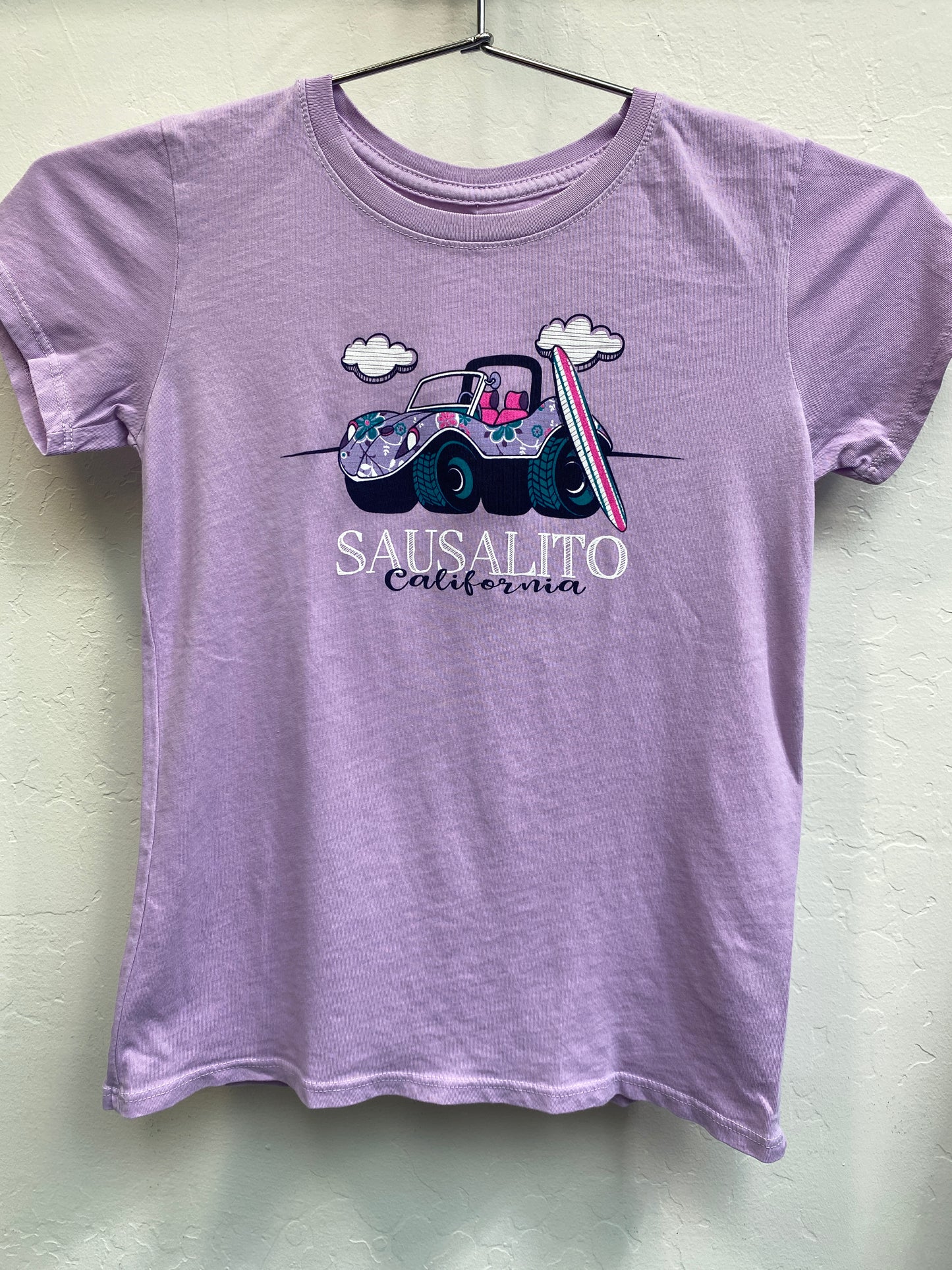 Purple kid's t-shirt with floral beach buggy and surfboard design, Sausalito California text, hanging on display